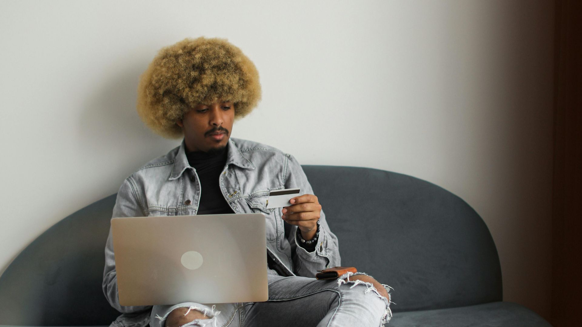 Man with afro hair using laptop and credit card for online shopping indoors.