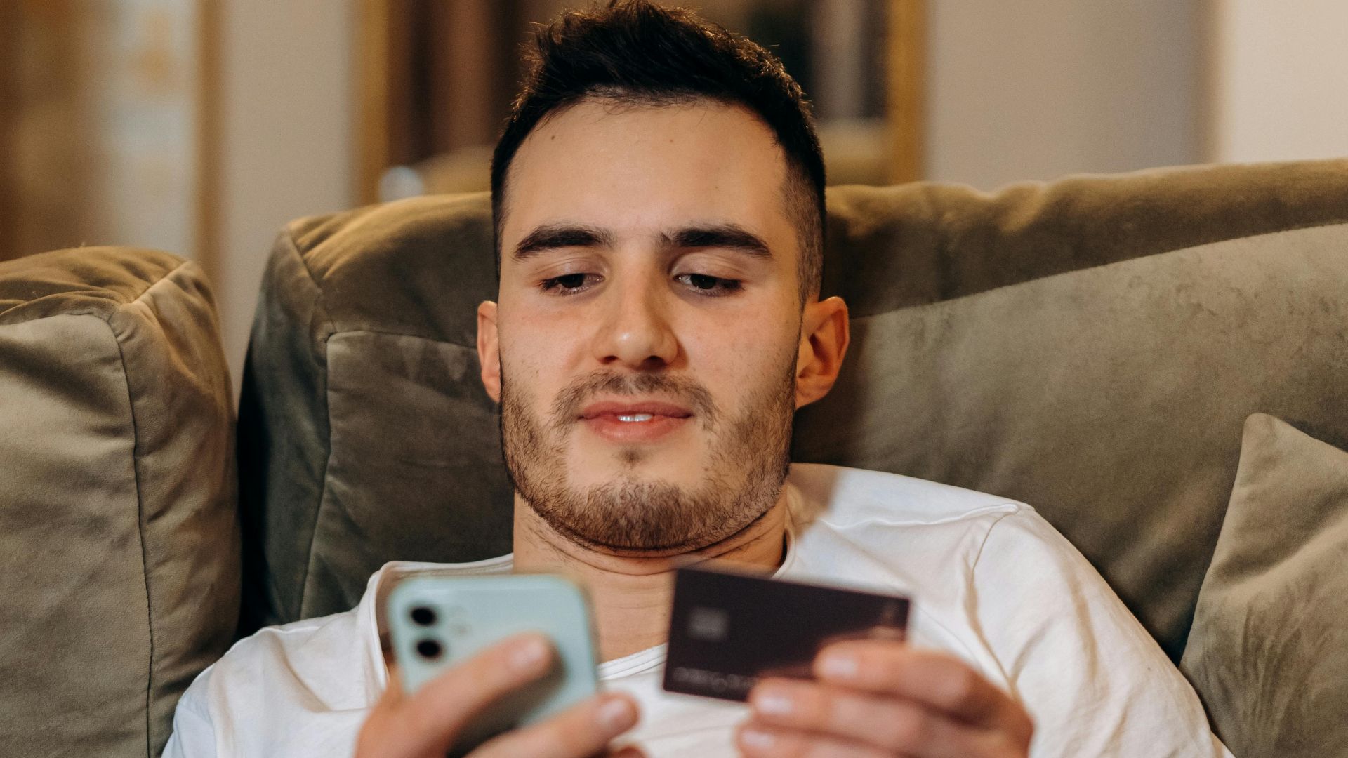 Young man using smartphone and credit card for online shopping indoors.