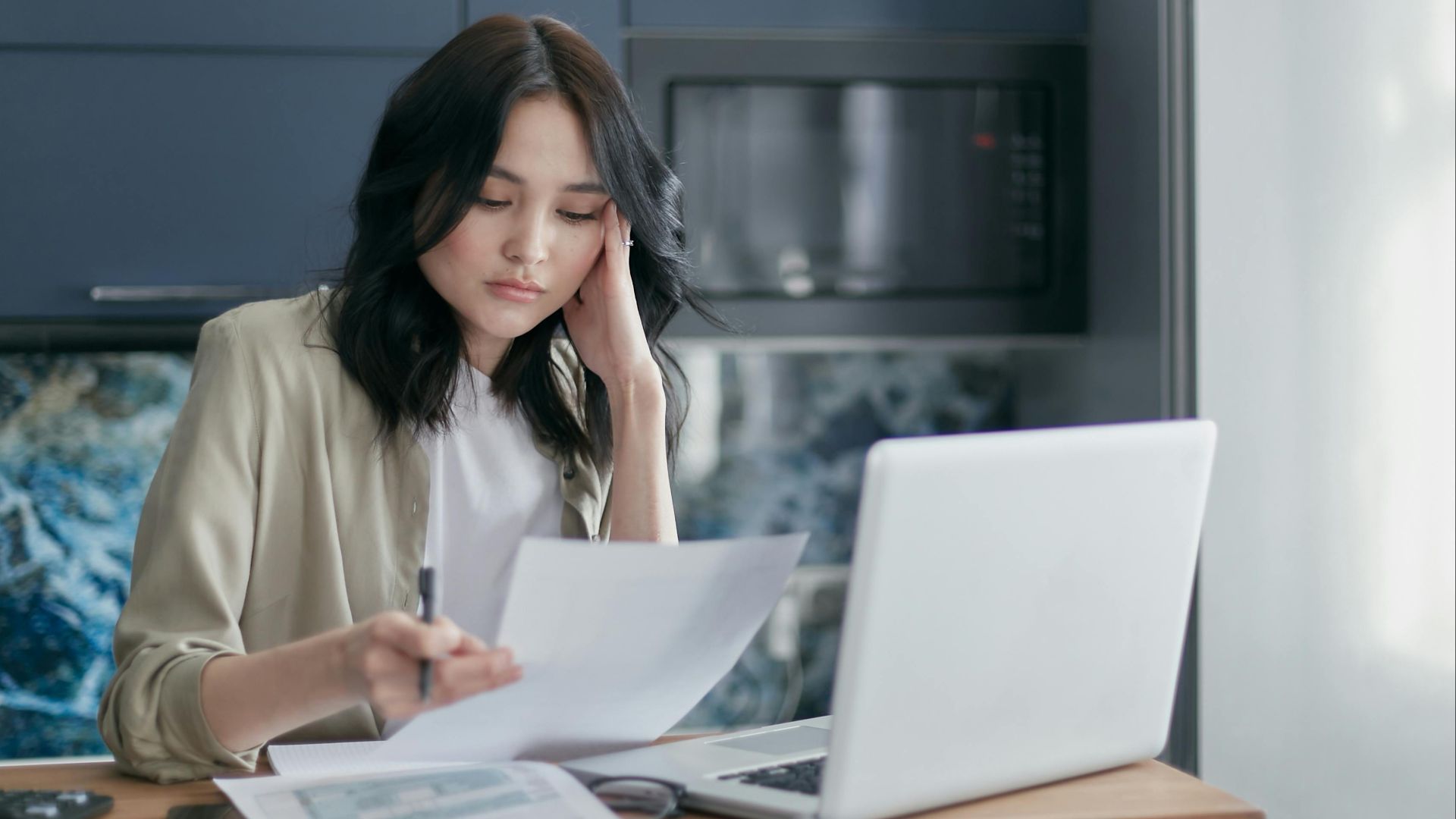 Focused young woman reviewing financial documents with a laptop in a home office setting.