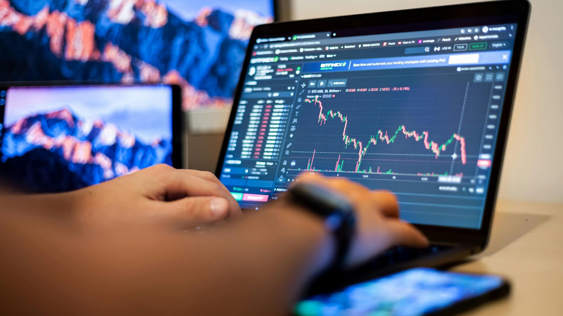 Hands typing on a laptop displaying financial trading charts, indicating active online trading work.