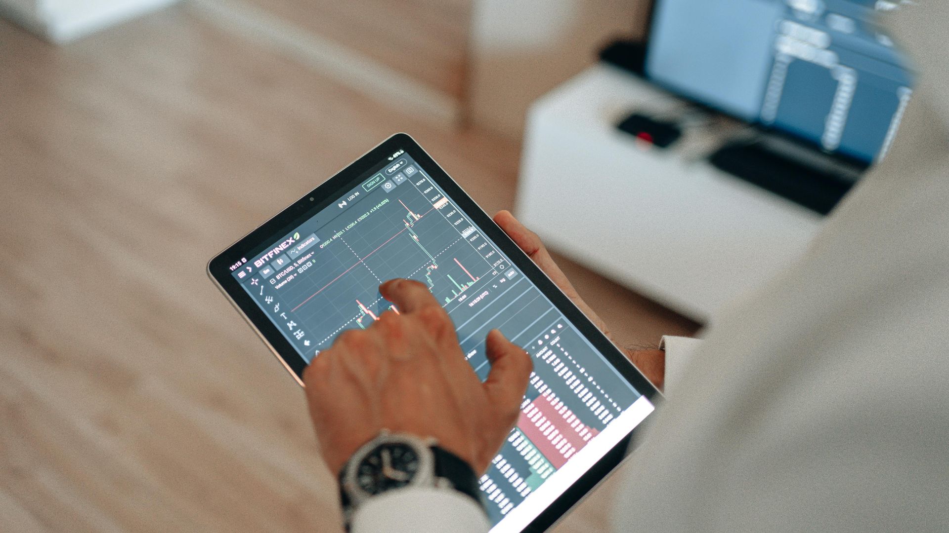 A person holding a tablet indoors displaying financial trading graphs, engaging in digital finance analysis.