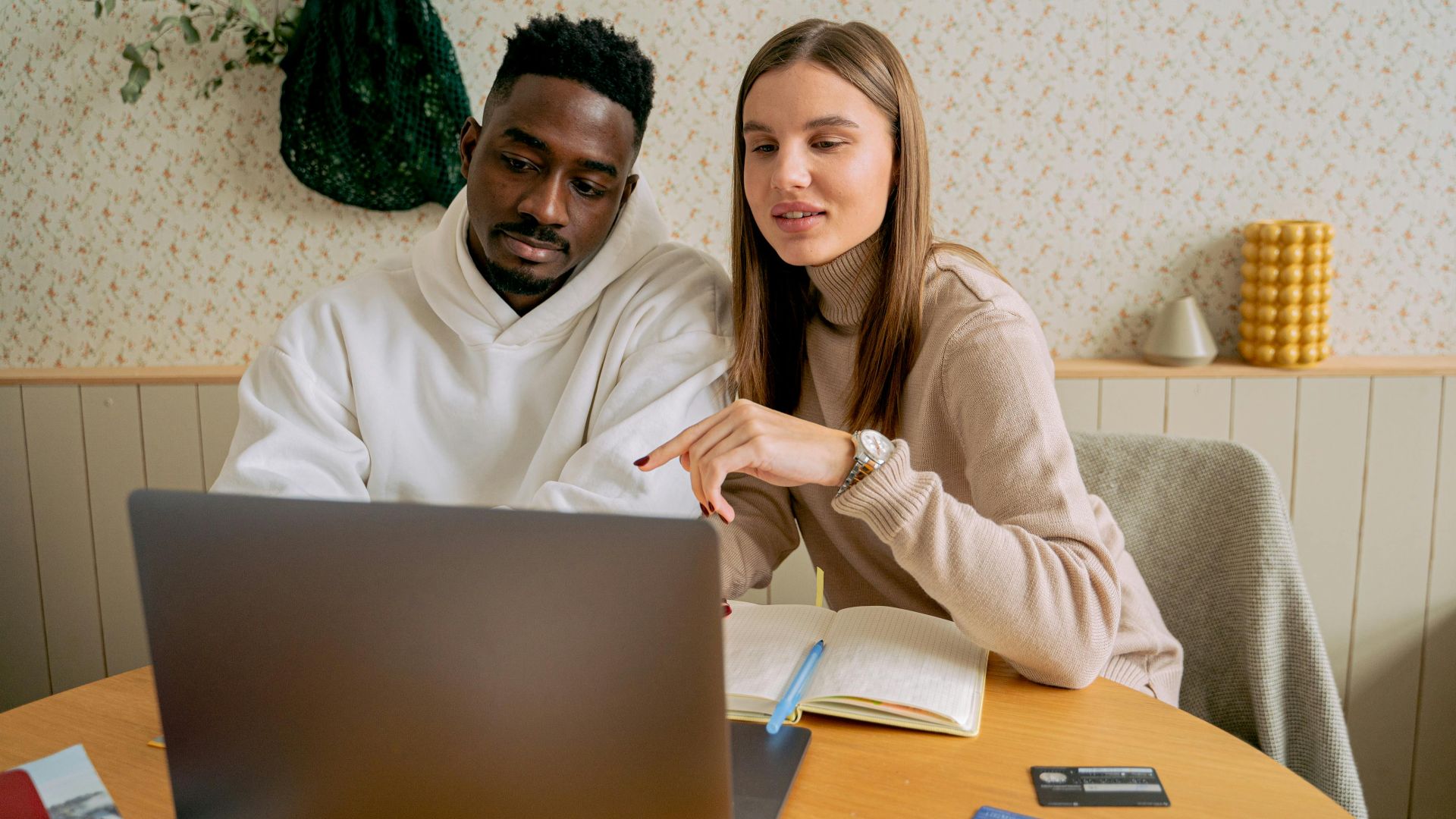 An interracial couple engaged in collaborative work on a laptop indoors, fostering teamwork.