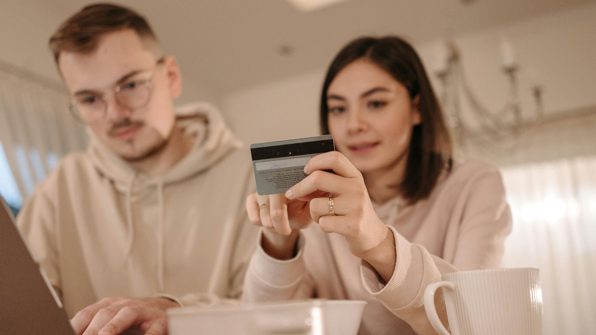 Young couple shopping online using a laptop and credit card at home, enjoying a cozy indoor setting.