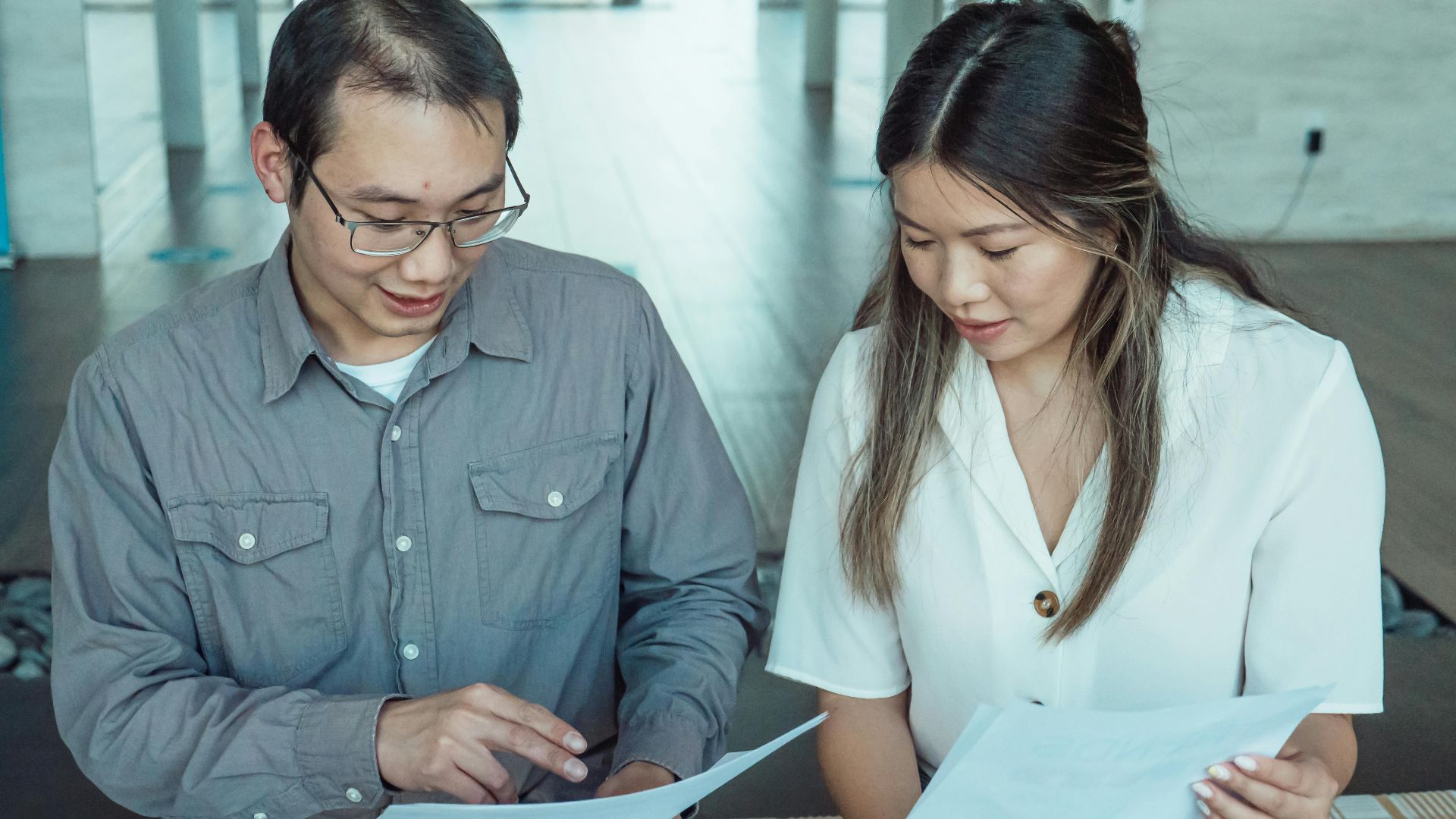 Two coworkers reviewing documents in a modern office, focused on teamwork and planning.