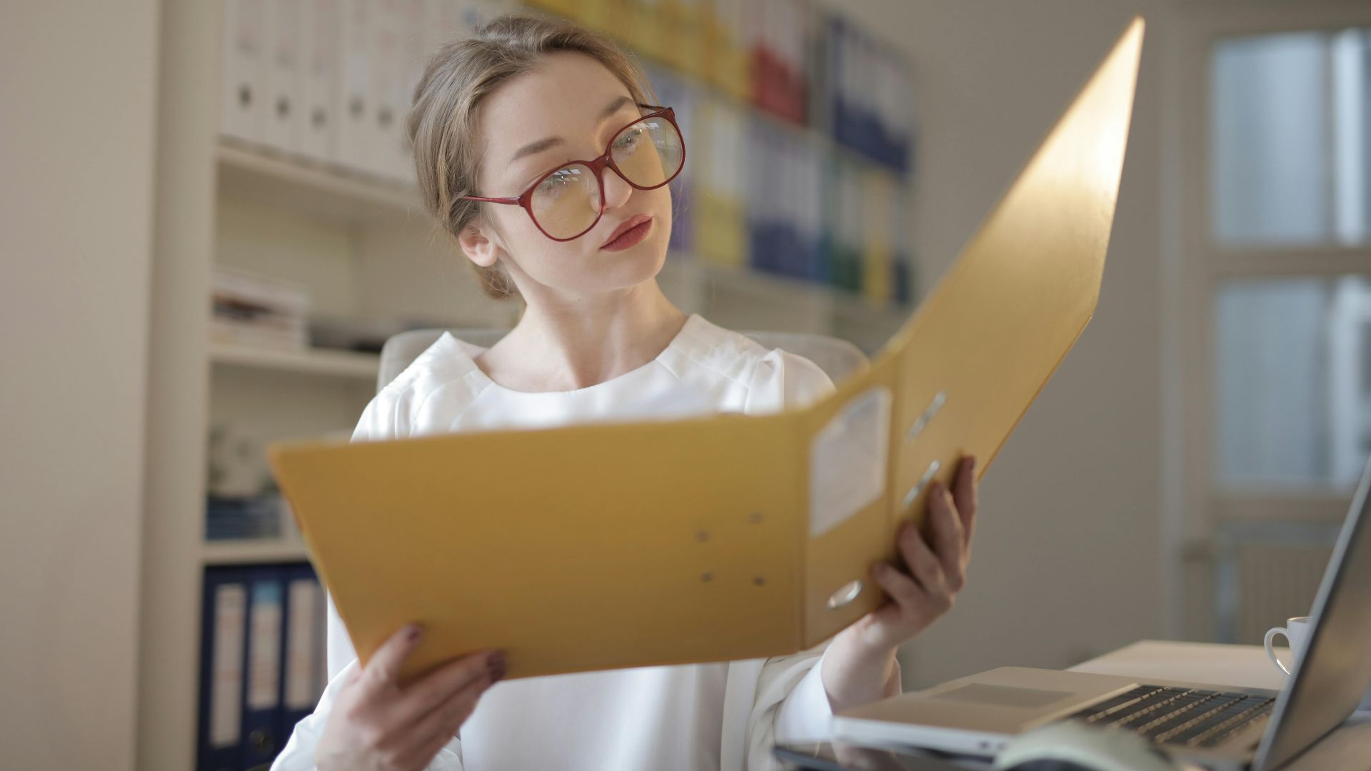 Caucasian woman intensely reading documents in an office setting.