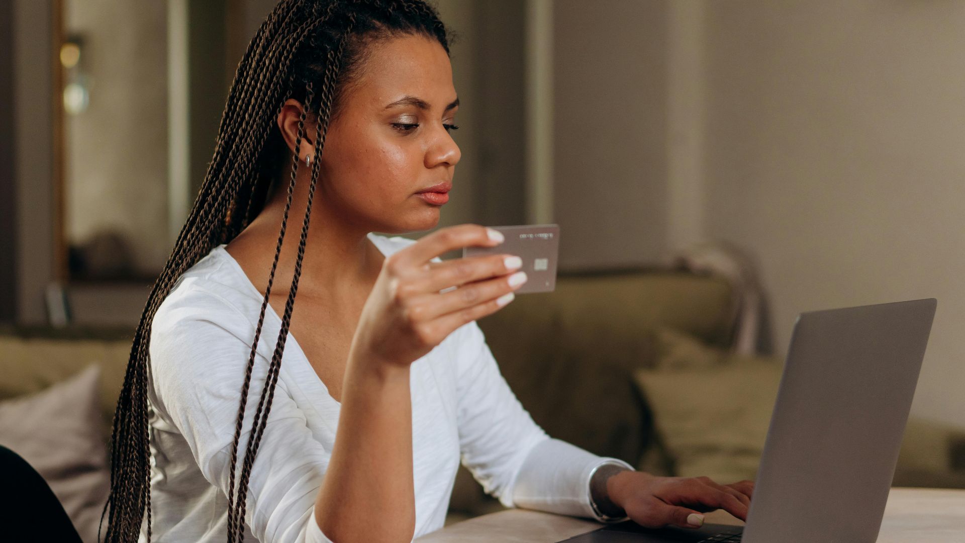 A woman with braided hair makes an online transaction using a credit card and laptop at home.
