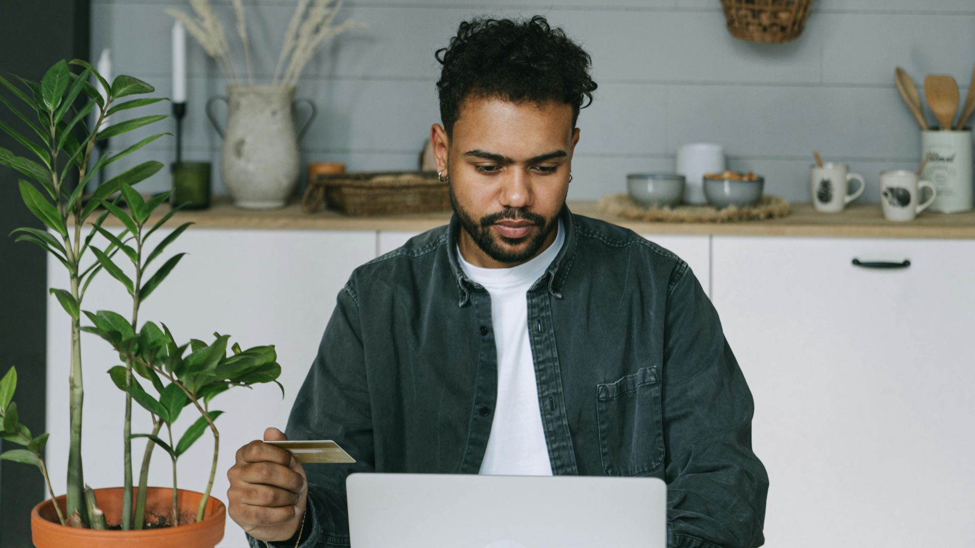 A man using a laptop and credit card for online shopping in a cozy indoor setting.