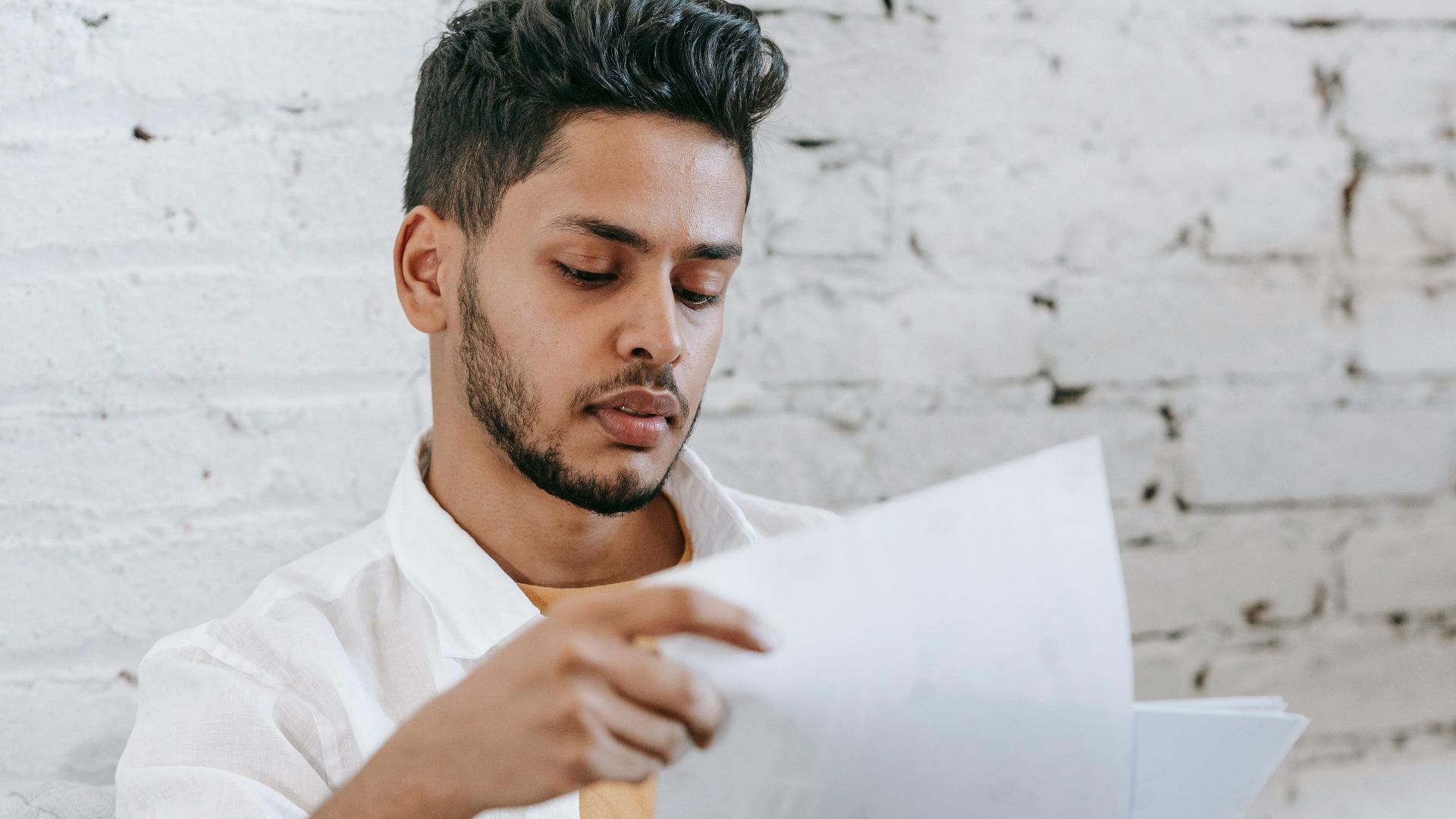 Young man attentively reviewing financial documents at home. Focused on paperwork.