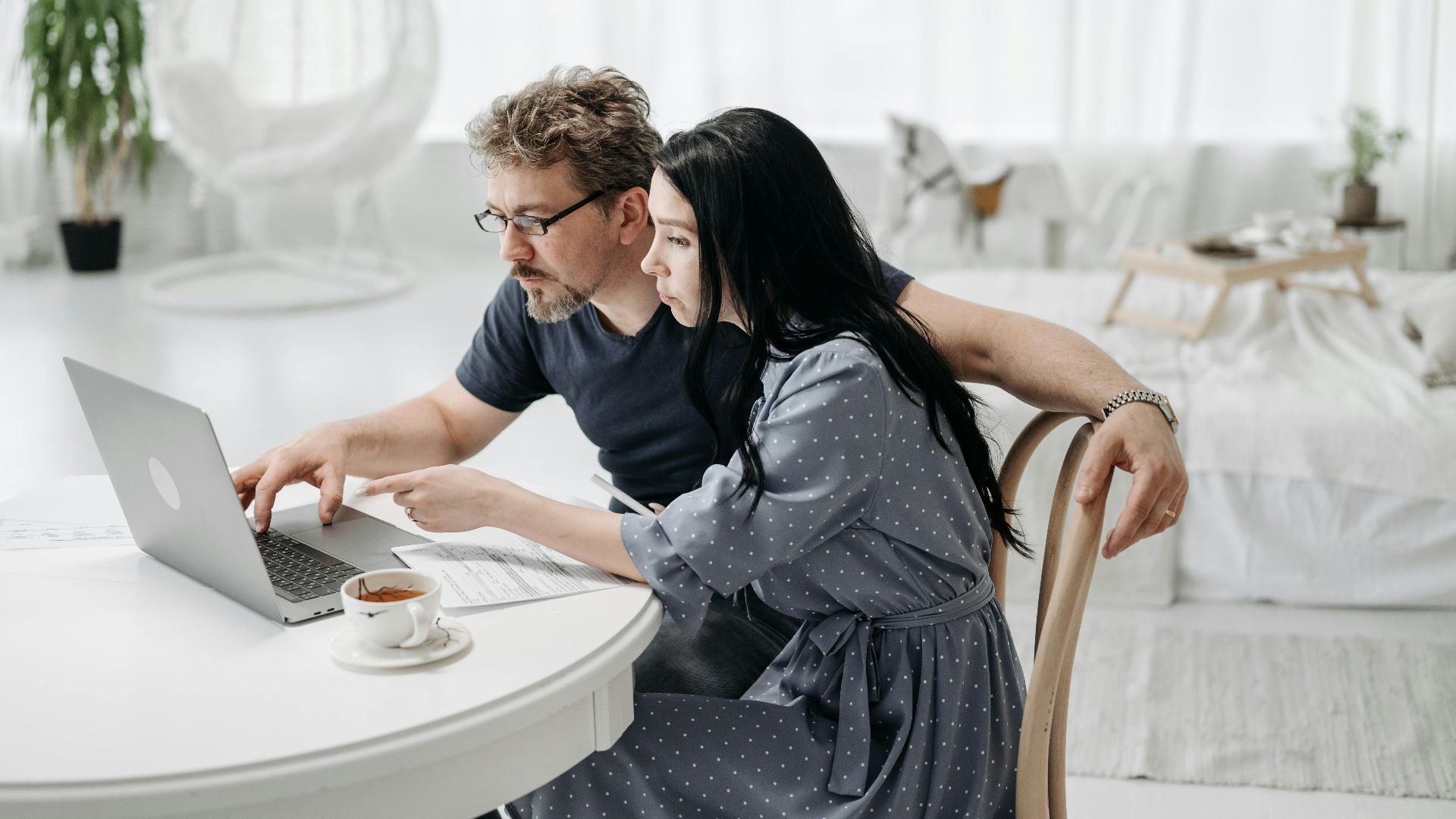 A man and woman sitting indoors, collaborating on a laptop at a table with coffee.