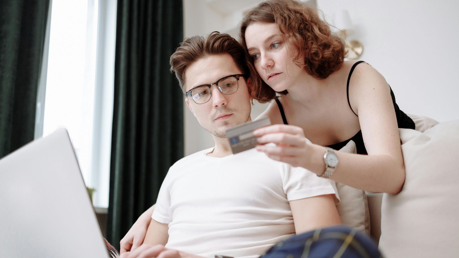 A young couple using a laptop and credit card for online shopping indoors.