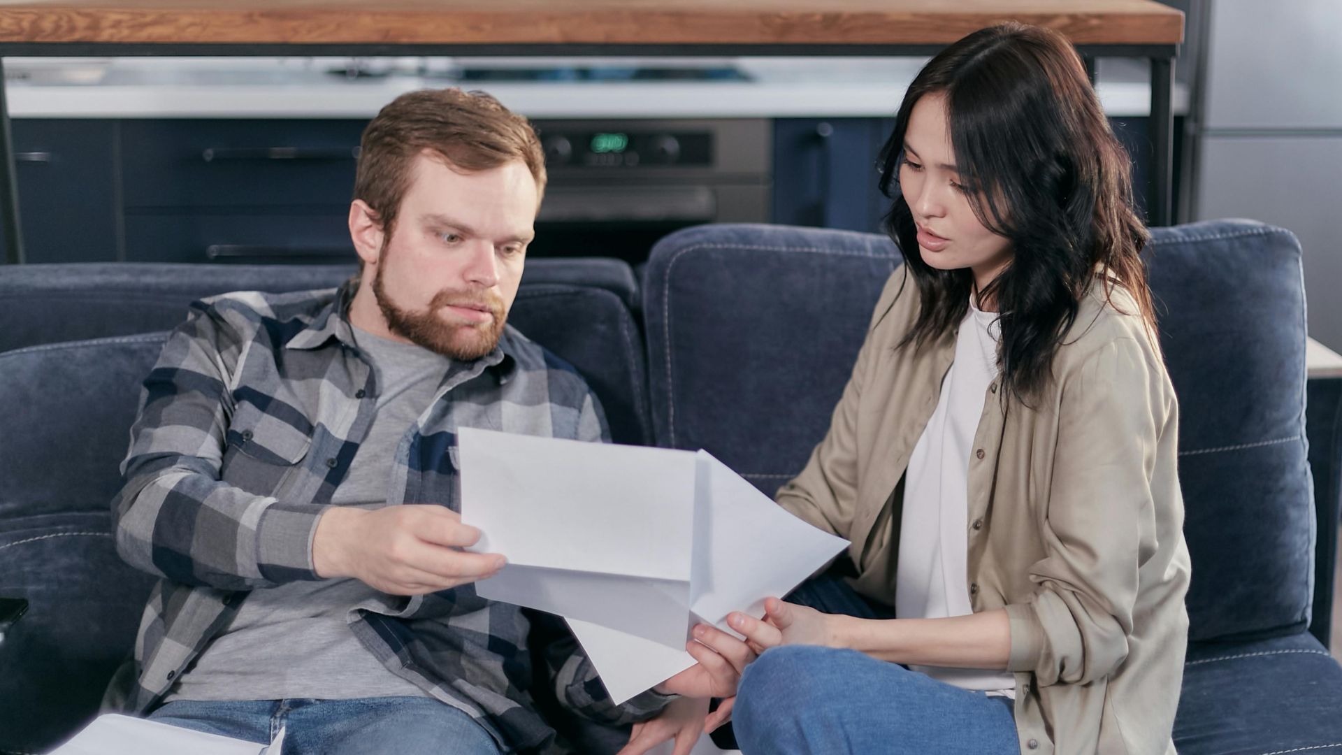 Asian woman and Caucasian man discussing taxes on couch.