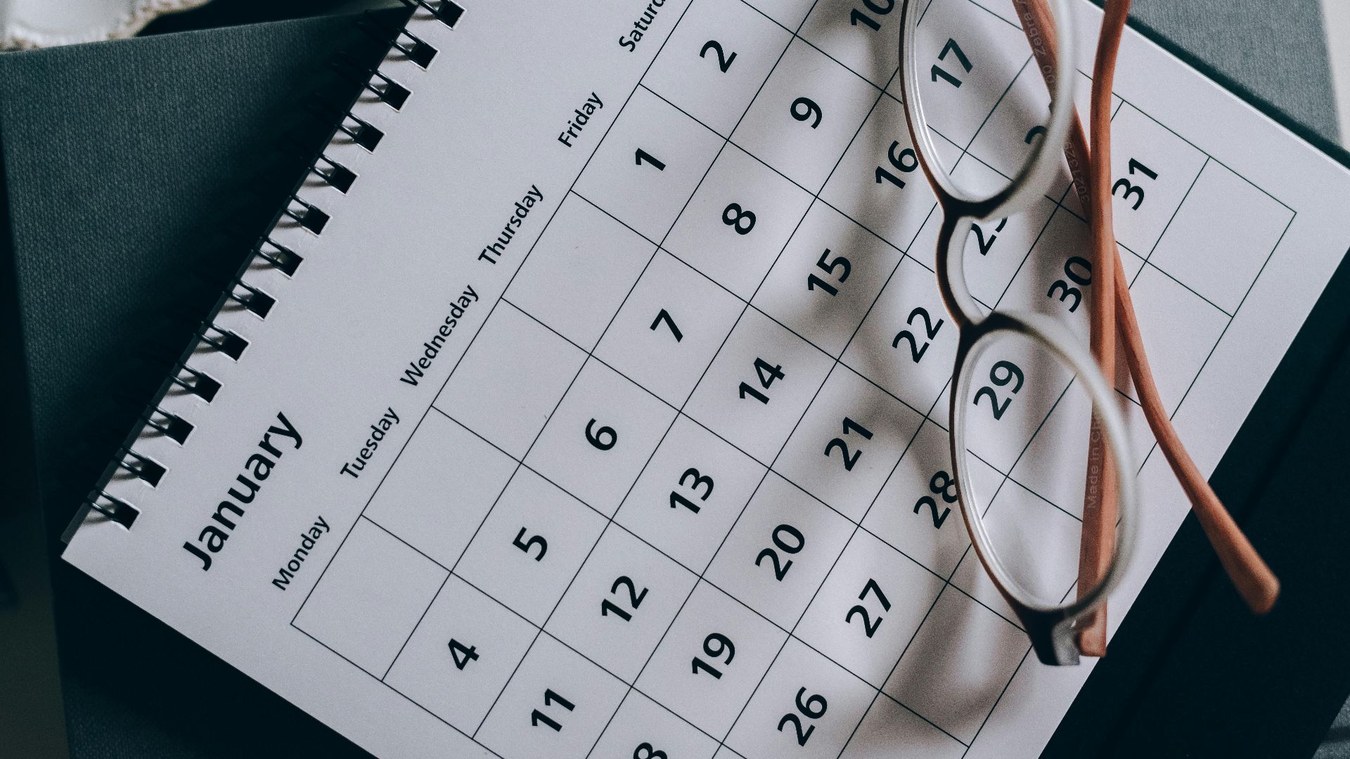 A close-up of a January calendar with eyeglasses on a table, emphasizing planning and organization.