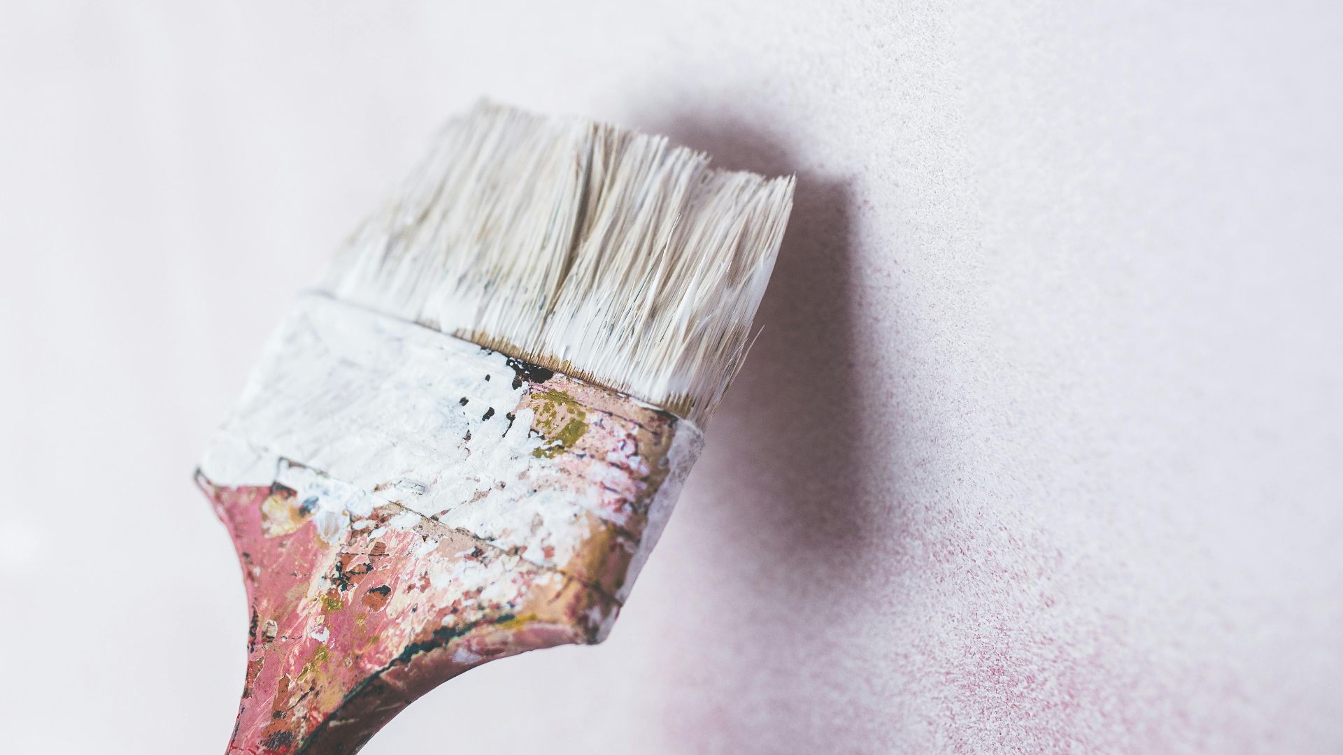 Close-up of a paintbrush applying white paint on a wall, showcasing a minimalist aesthetic.