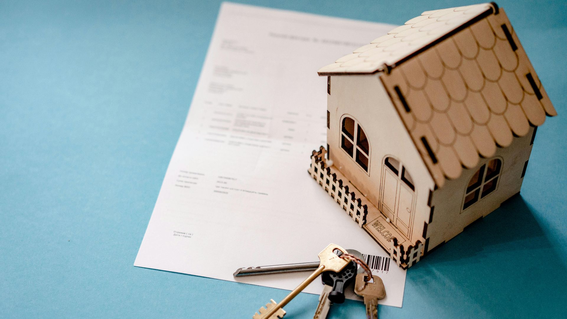 Miniature wooden house with keys and contract symbolizing real estate transactions.