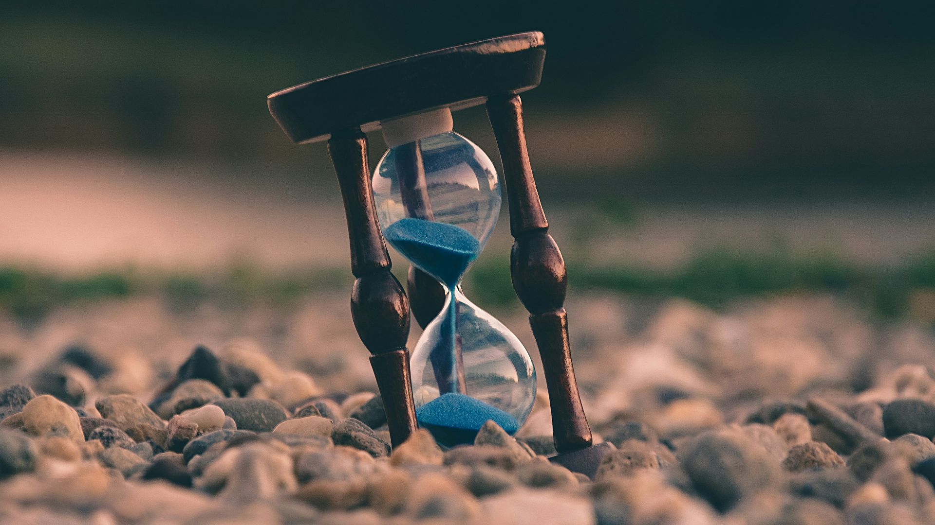 selective focus photo of brown and blue hourglass on stones
