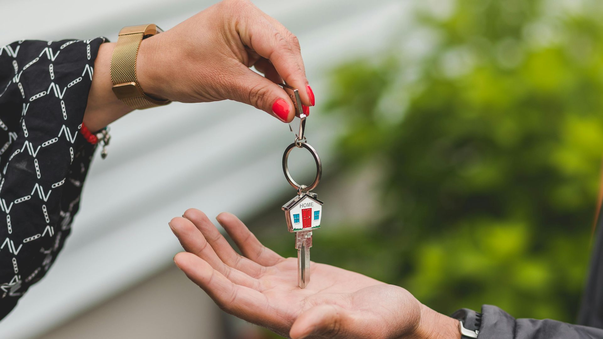 Close-up of a hand handing over a key with a house keychain, symbolizing real estate transaction.