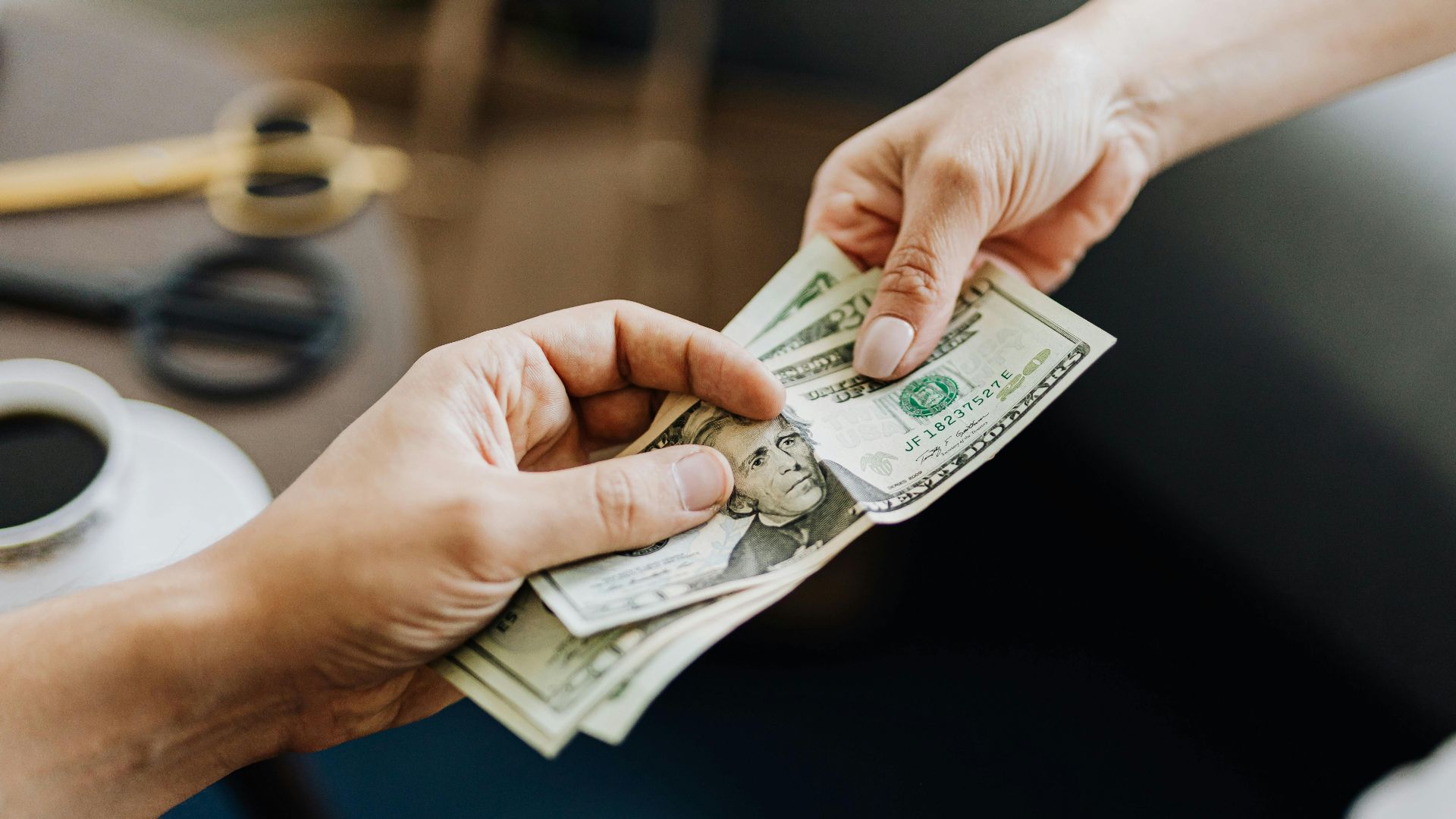 A close-up image of hands exchanging US dollar bills, symbolizing financial transaction or payment.