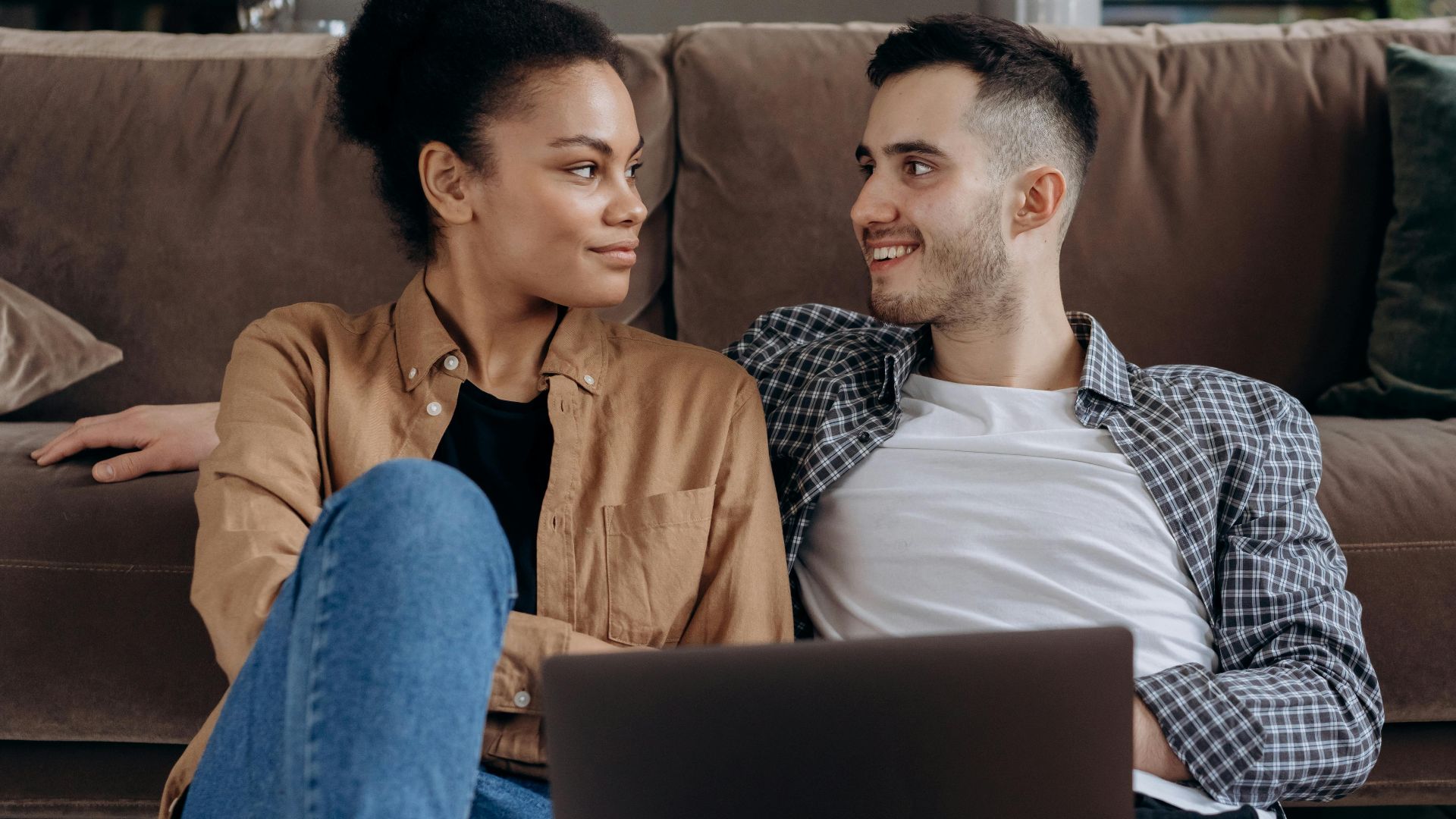Happy couple sitting together on a couch with a laptop, enjoying each other's company.