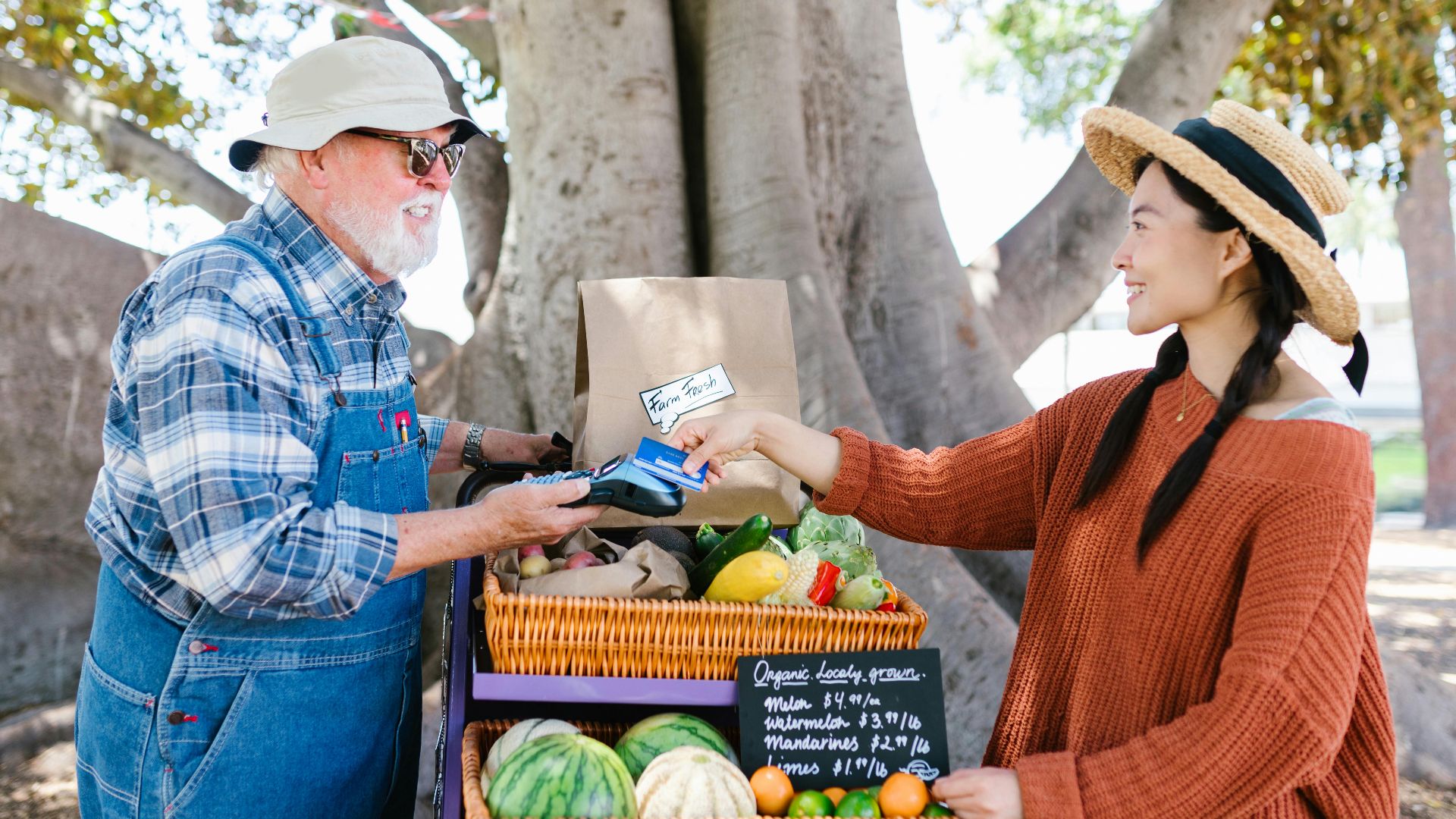 A cheerful exchange at an outdoor farmer's market with fresh produce displayed.