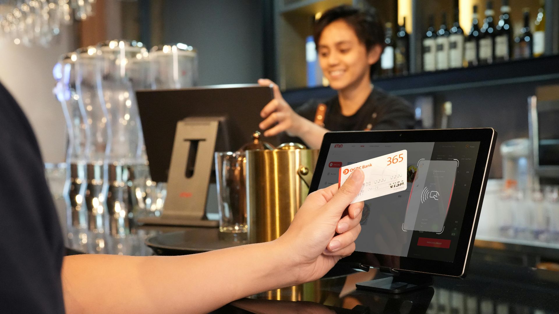 Person using contactless credit card payment at a modern bar, assisted by a cashier.