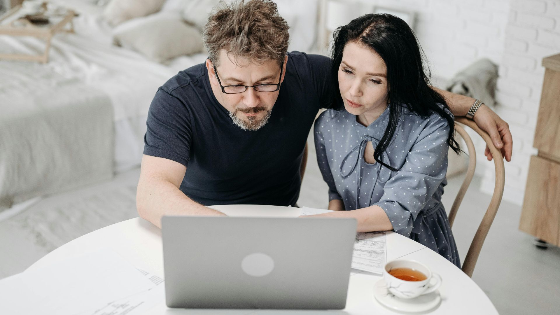 Couple working together on a laptop at home, discussing plans over tea.
