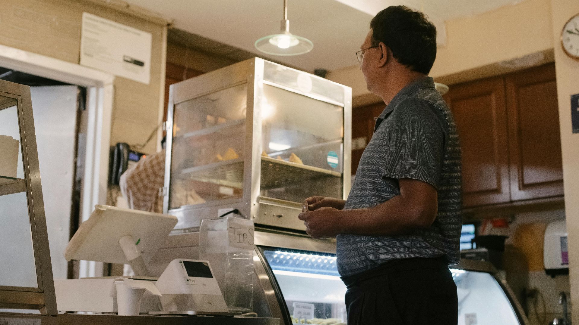 Side view of ethnic male wearing casual clothes standing near showcase and cash register while buying food in grocery store