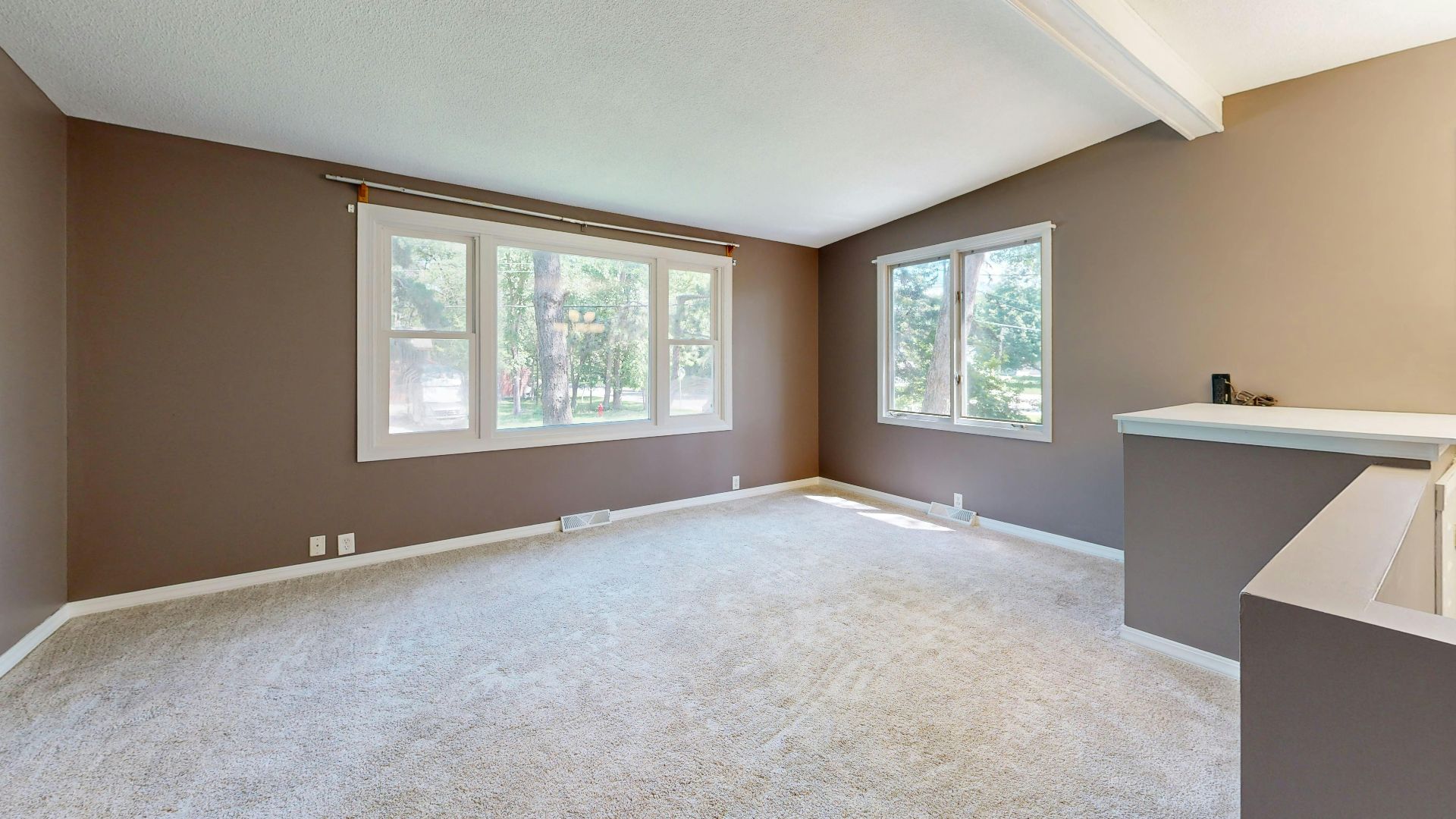 Large empty living room with neutral walls and carpet, natural light through windows.