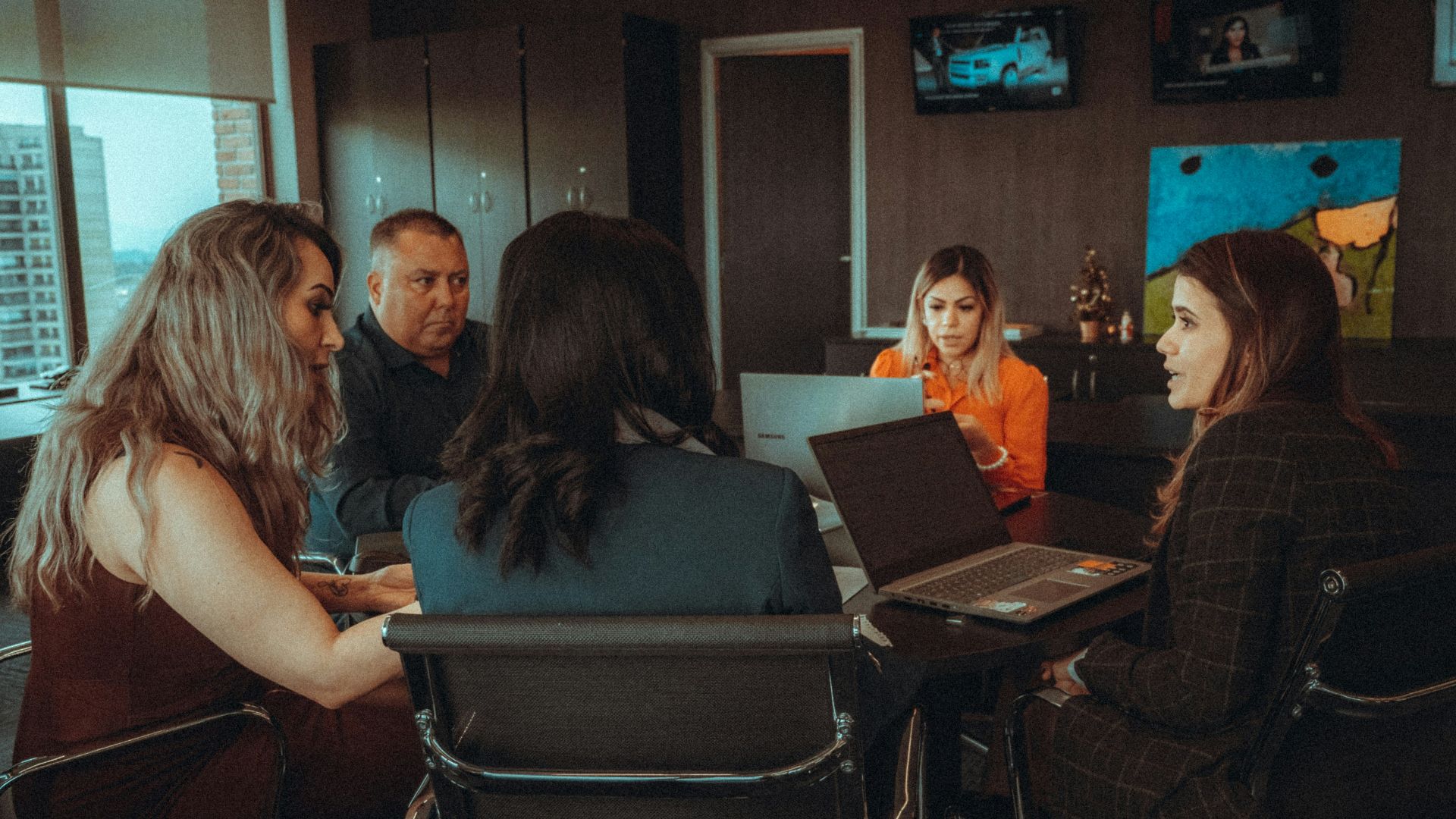 a group of people sitting around a table with laptops