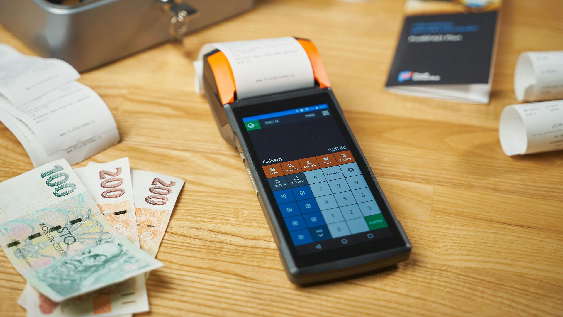 A modern digital payment terminal on a wooden desk with cash and receipts.