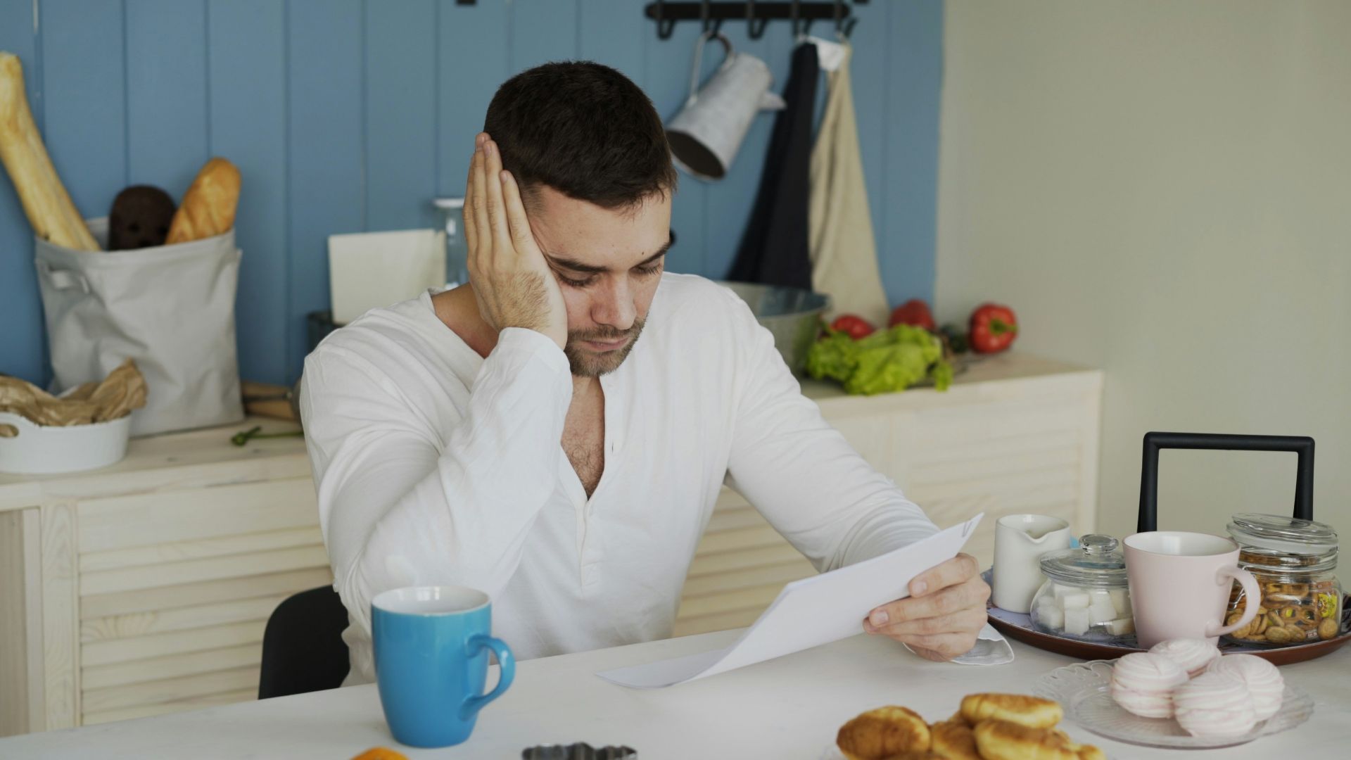 Man sitting at table reading papers with breakfast.