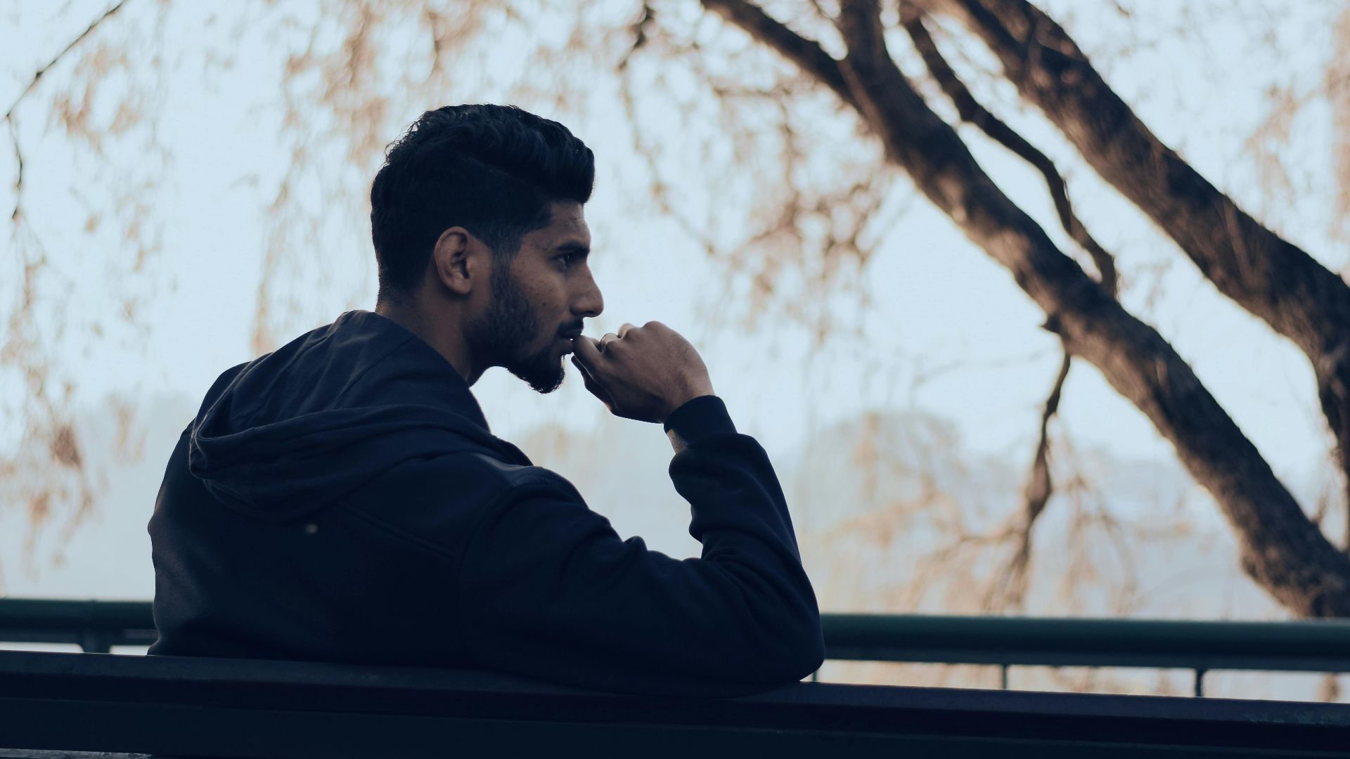Man in deep thought sitting on a bench in a serene autumn park setting.