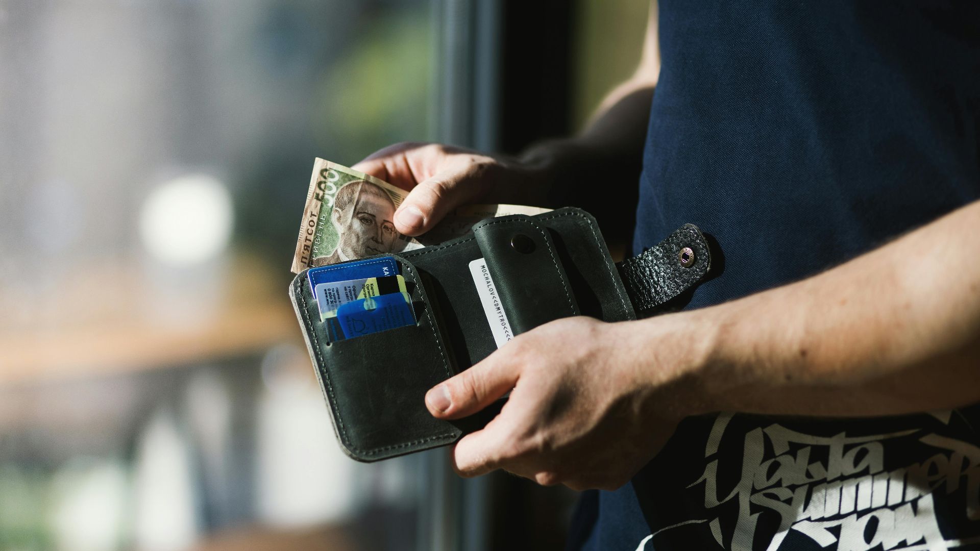 Close-up of a man holding a wallet with cash and credit cards, indoors.