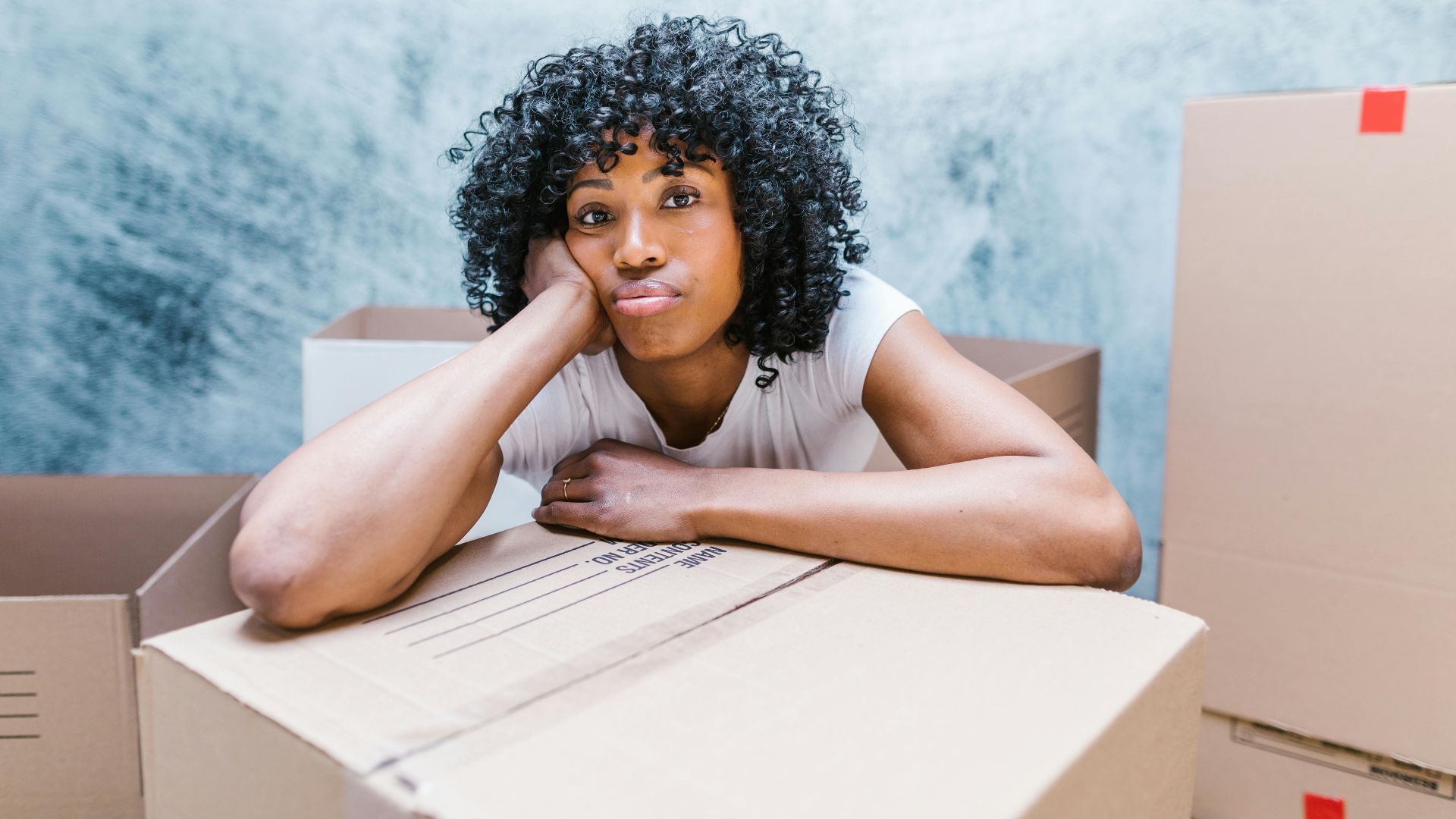 Tired woman leaning on a moving box while packing and relocating to a new home.