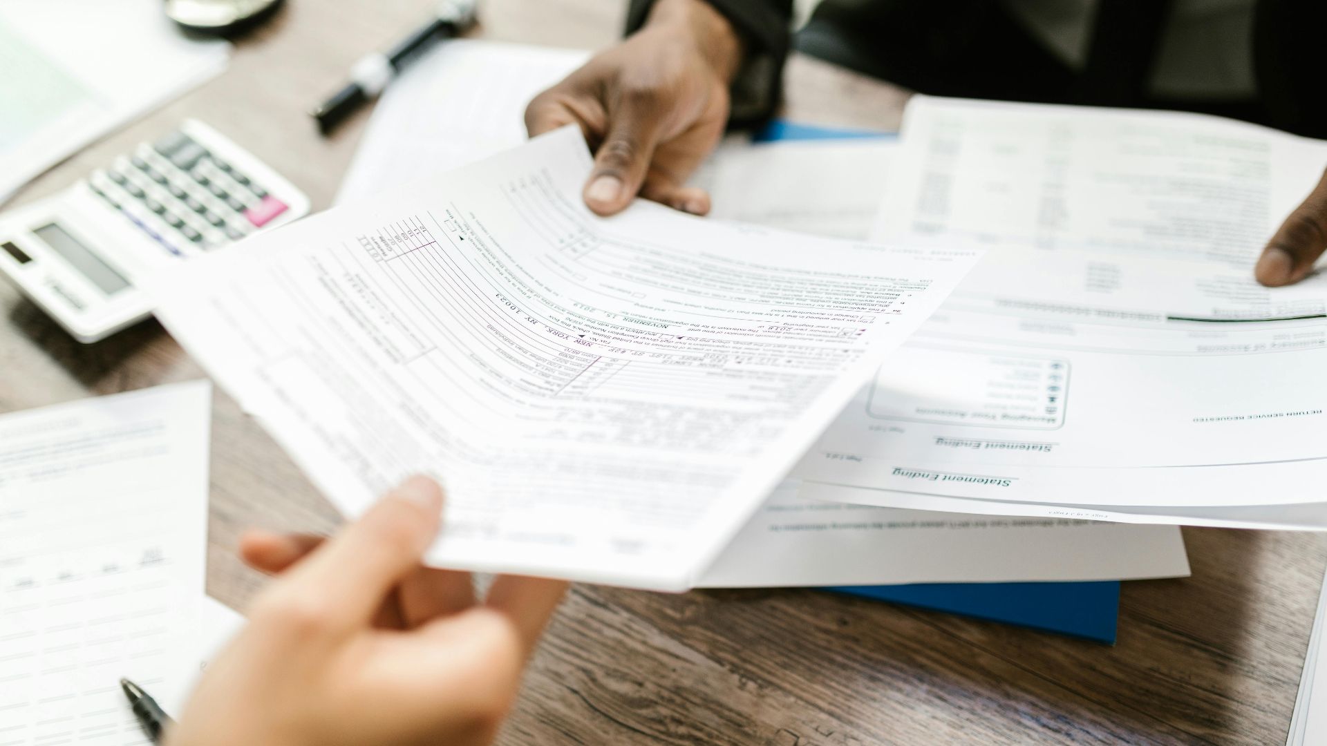 Two professionals exchanging documents in an office setting, focusing on paperwork and data analysis.