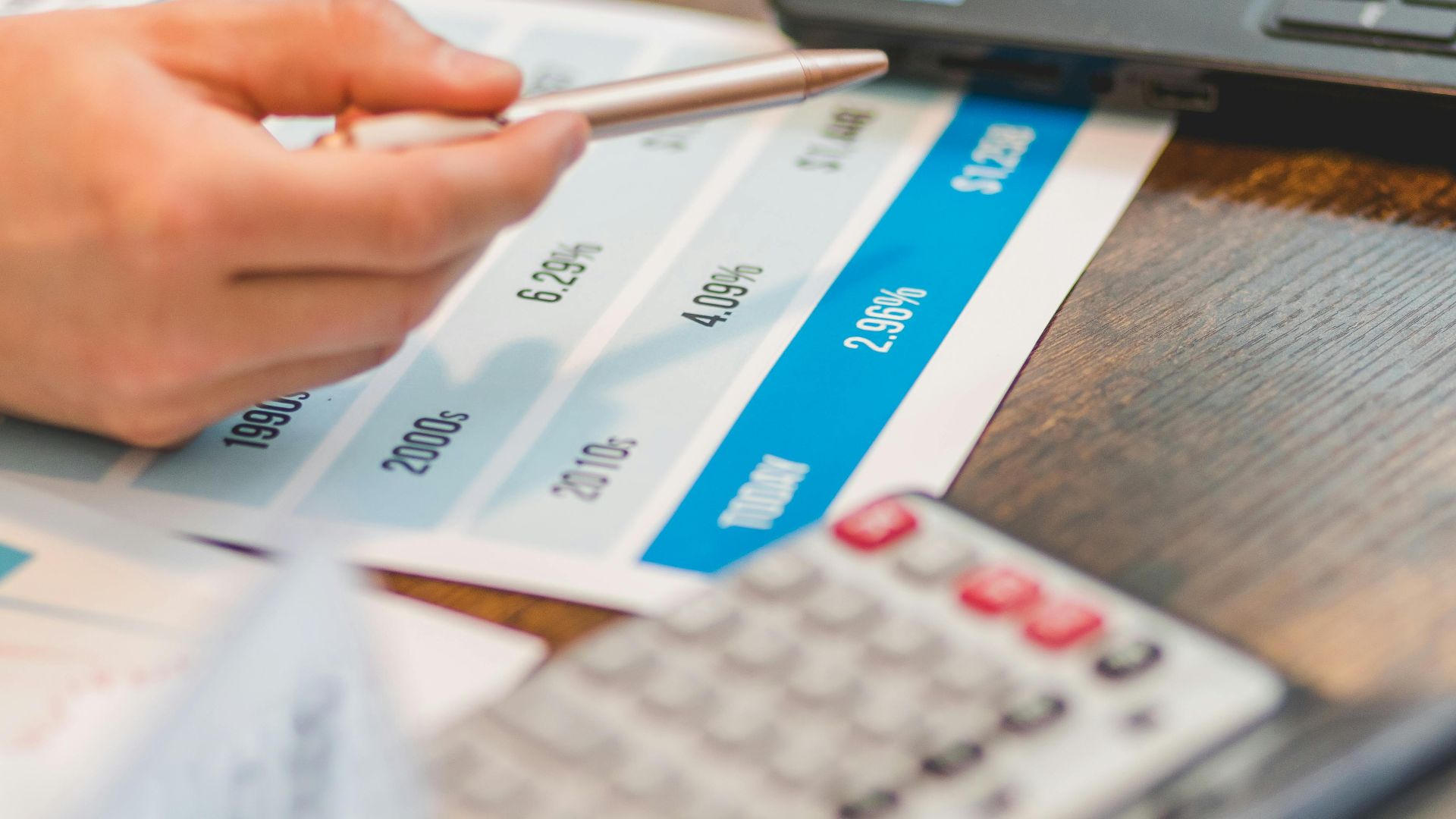 Close-up of a hand using a ballpen and calculator to analyze interest rates on a chart.