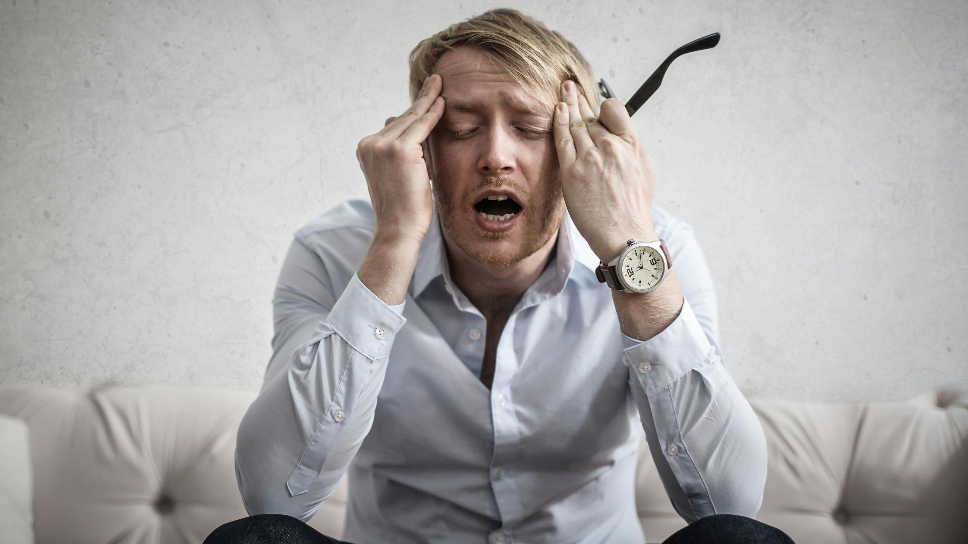 Stressed man sitting on couch, feeling overwhelmed and frustrated, expressing mental strain.