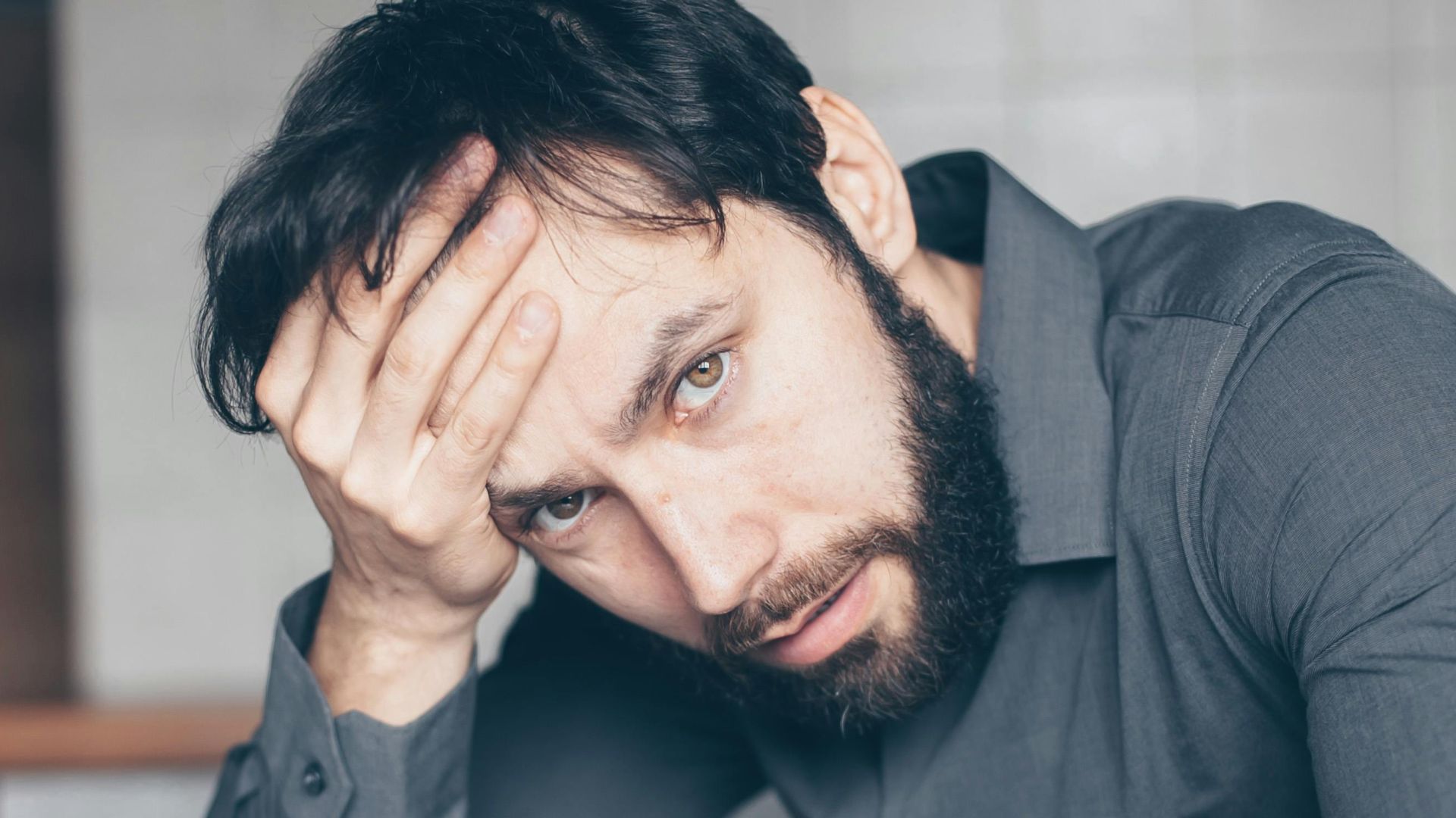Thoughtful man sitting at a table with glasses and cup, showing frustration.
