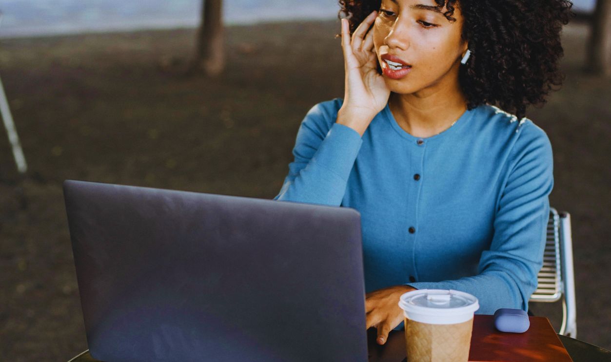 Photograph of a Woman Touching Her Ear while Working on Her Laptop