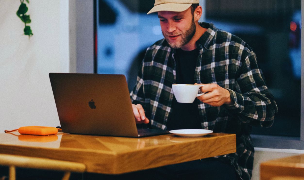 man sitting while having coffee and using laptop