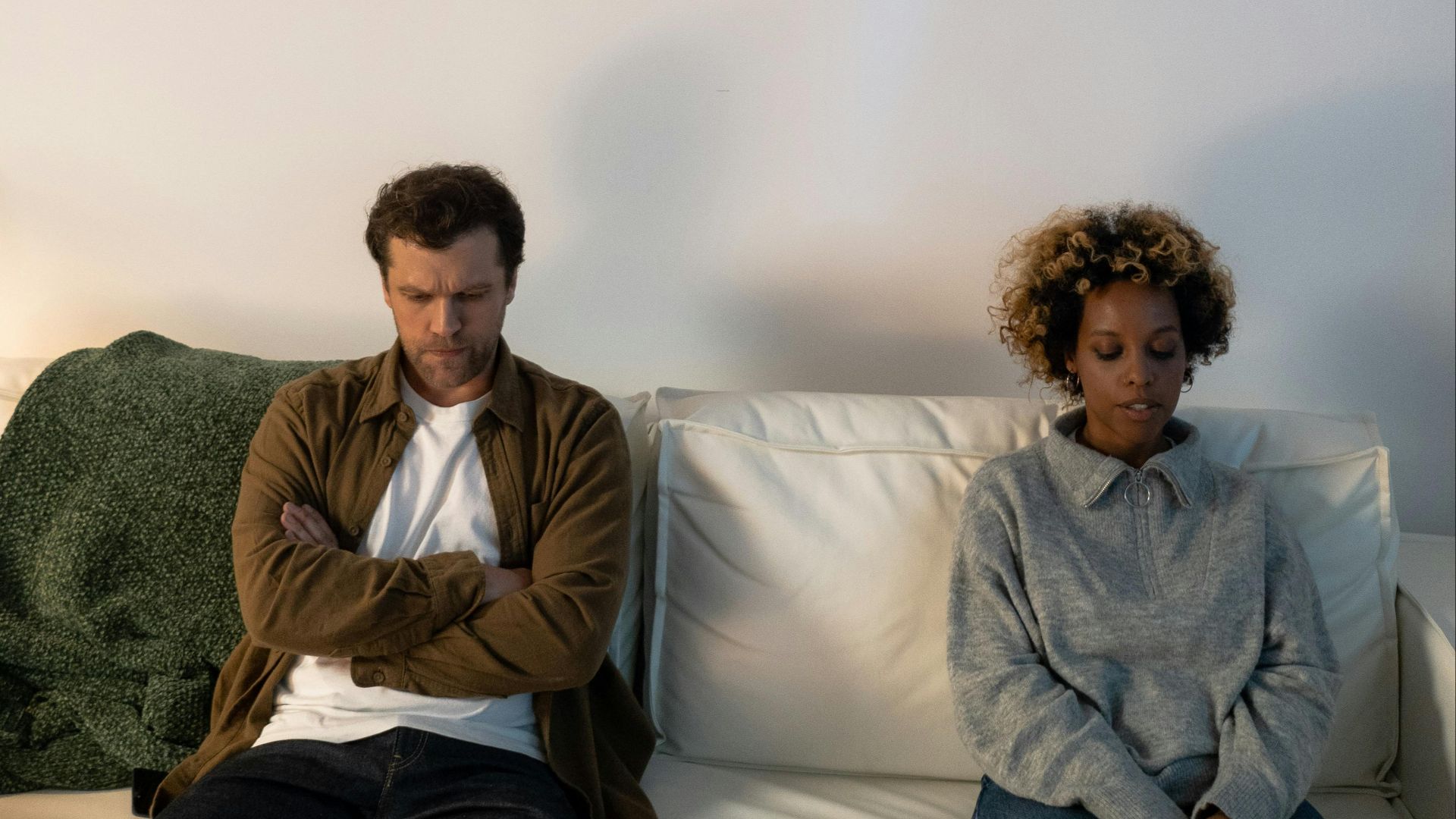 A couple experiencing tension, sitting apart on a sofa indoors.