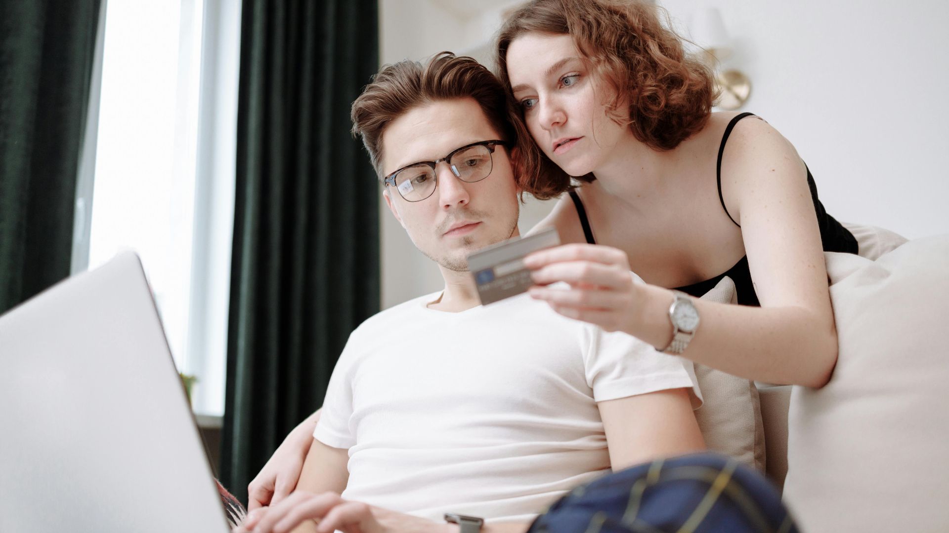 A young couple using a laptop and credit card for online shopping indoors.