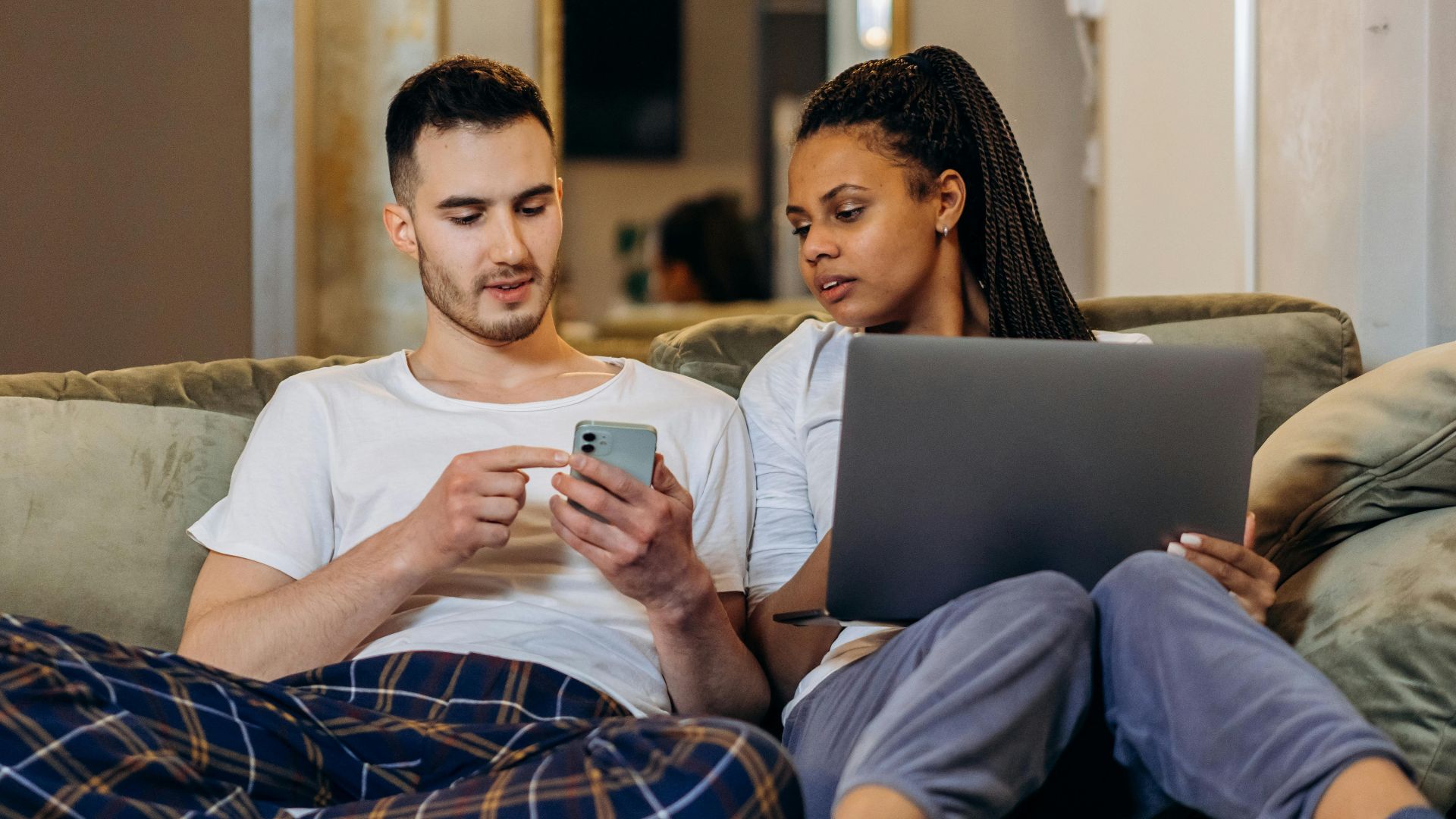 A couple sitting together on a couch, using a laptop and smartphone, enjoying a cozy moment.