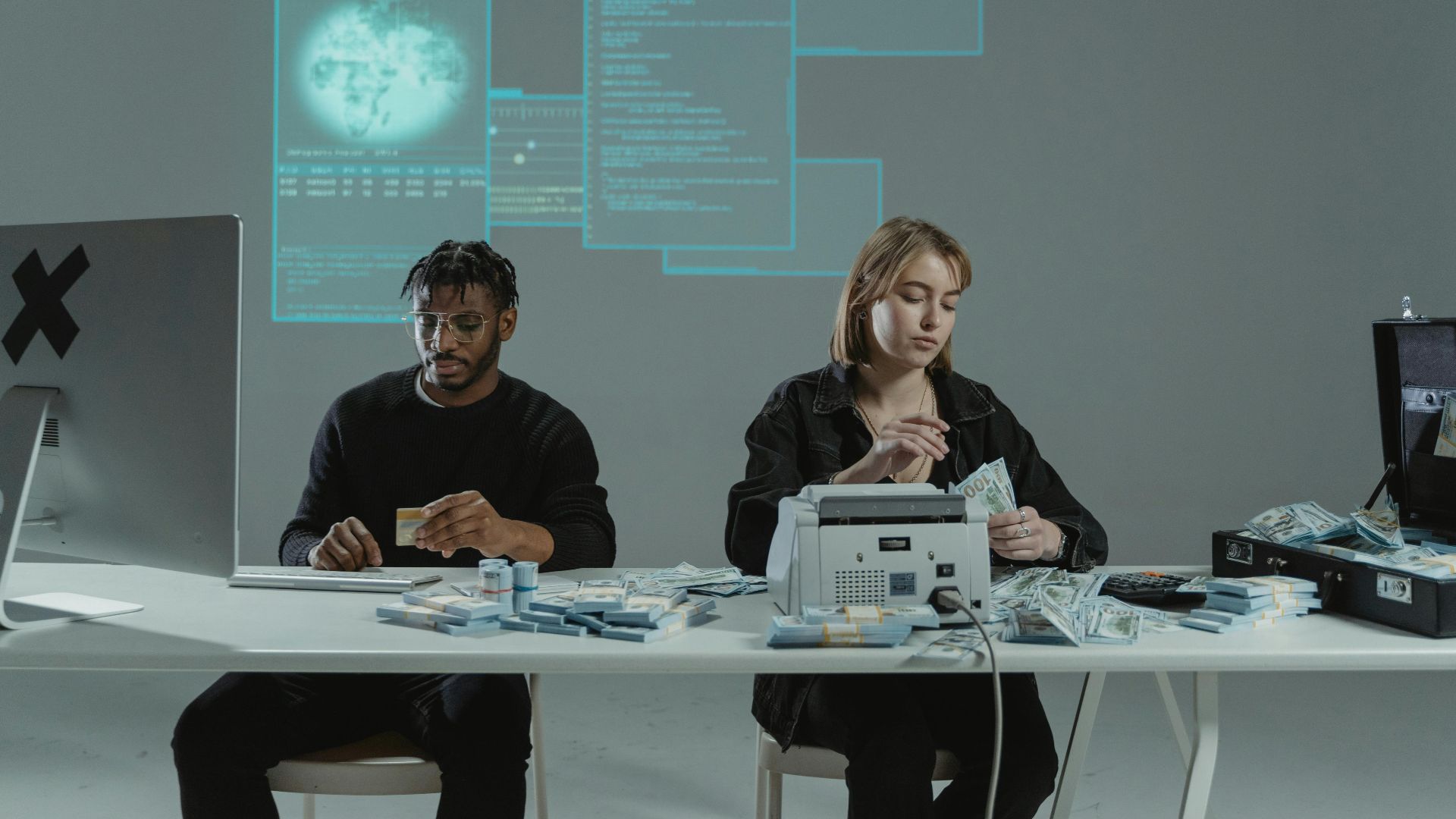 Two adults counting money in an office with a tech-themed background.