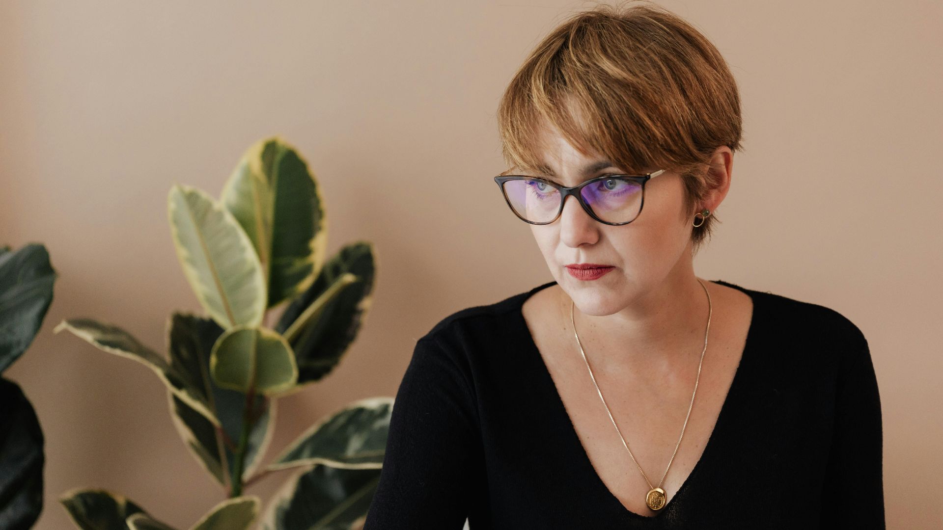 A thoughtful young woman with eyeglasses working in a modern office environment.
