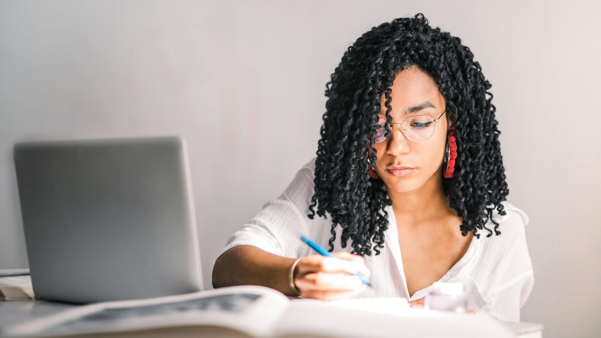 Focused young woman working at a desk with a laptop and writing notes.