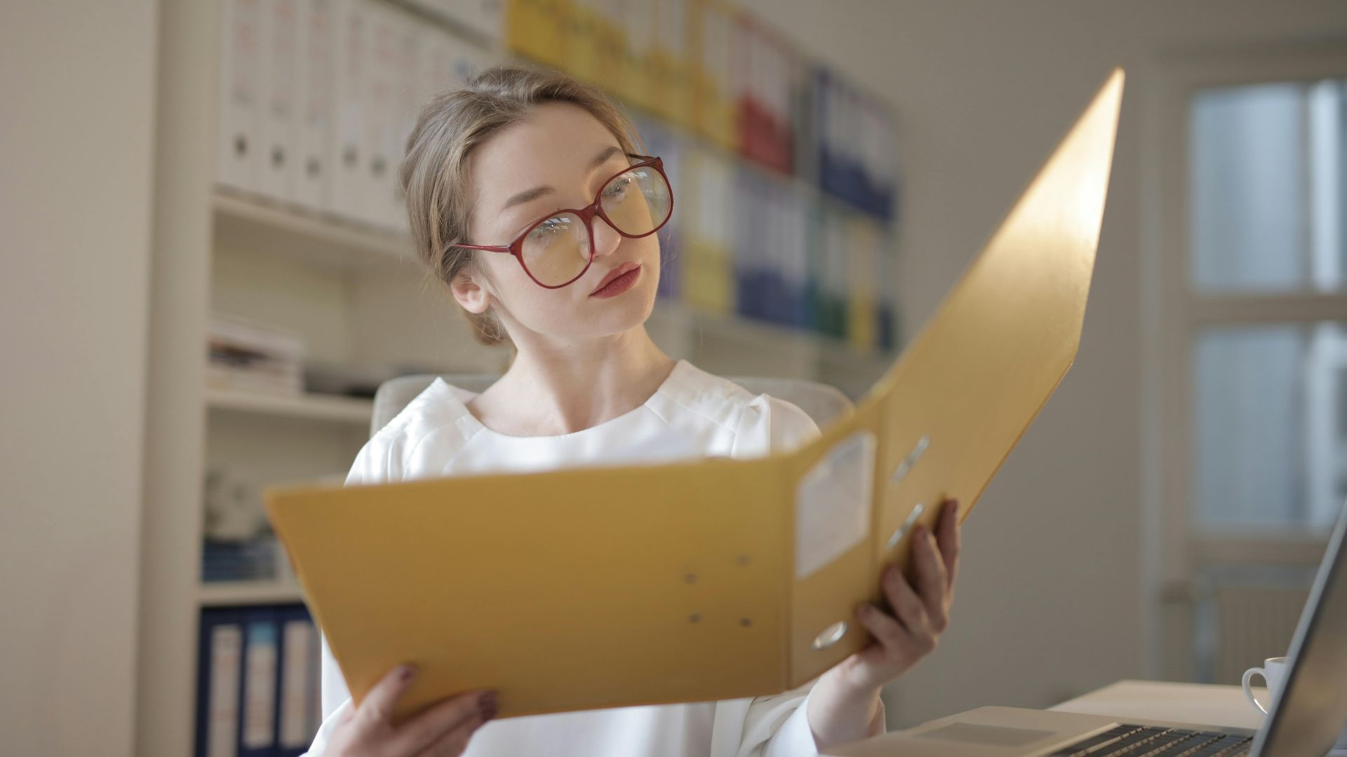 Caucasian woman intensely reading documents in an office setting.