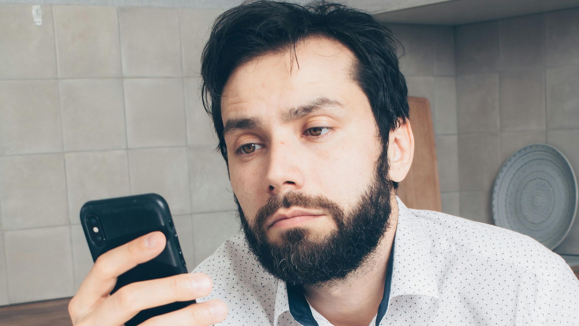 A man looks frustrated while checking his smartphone, possibly experiencing a banking issue or scam.
