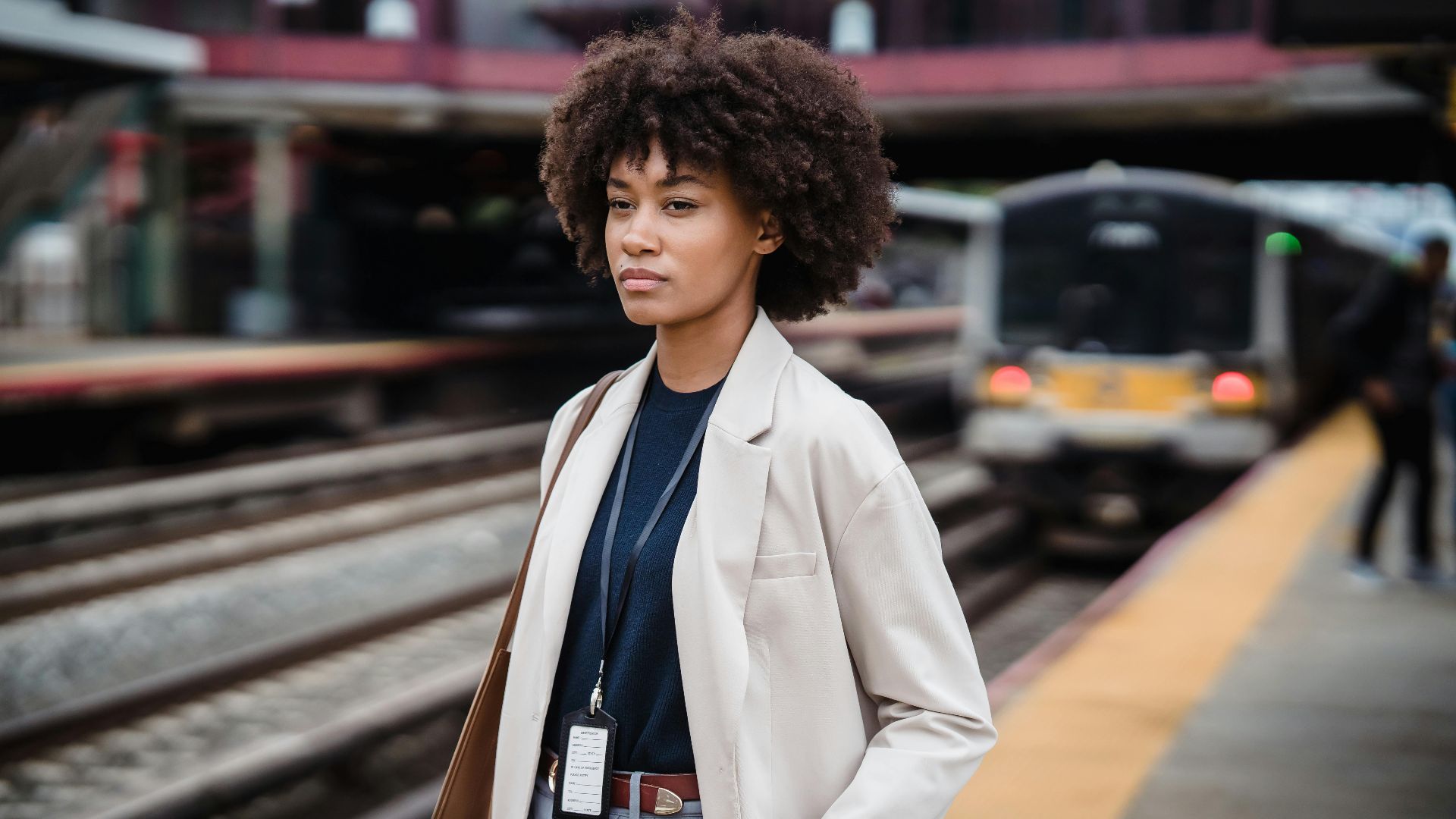A woman with curly hair stands at a train station, waiting for public transportation.