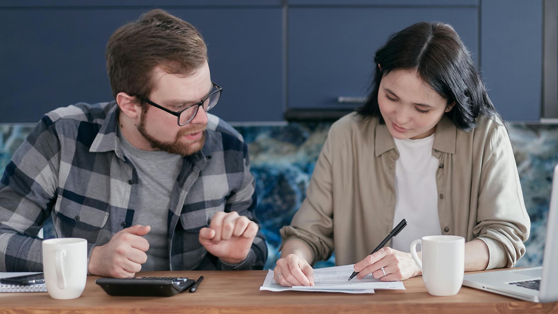 A couple sitting at a table managing their finances with a laptop and calculator, appearing focused.