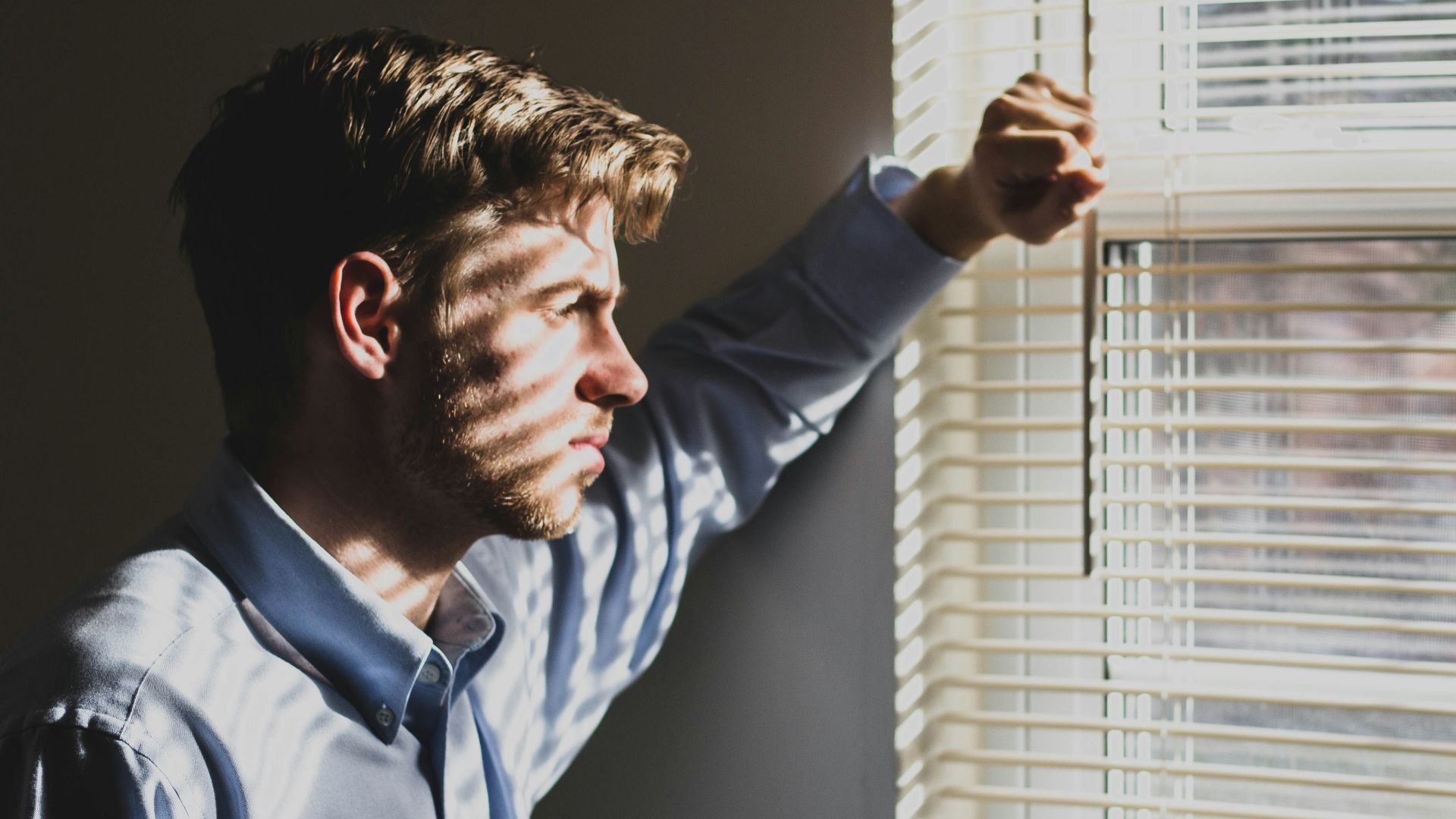 person near clear glass window pane and window blinds low-light photography